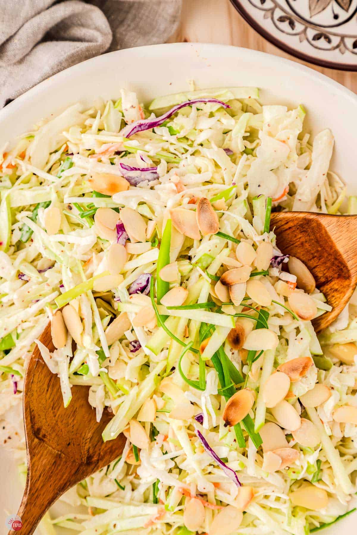 two wood spoons in a bowl of cabbage and apple slaw
