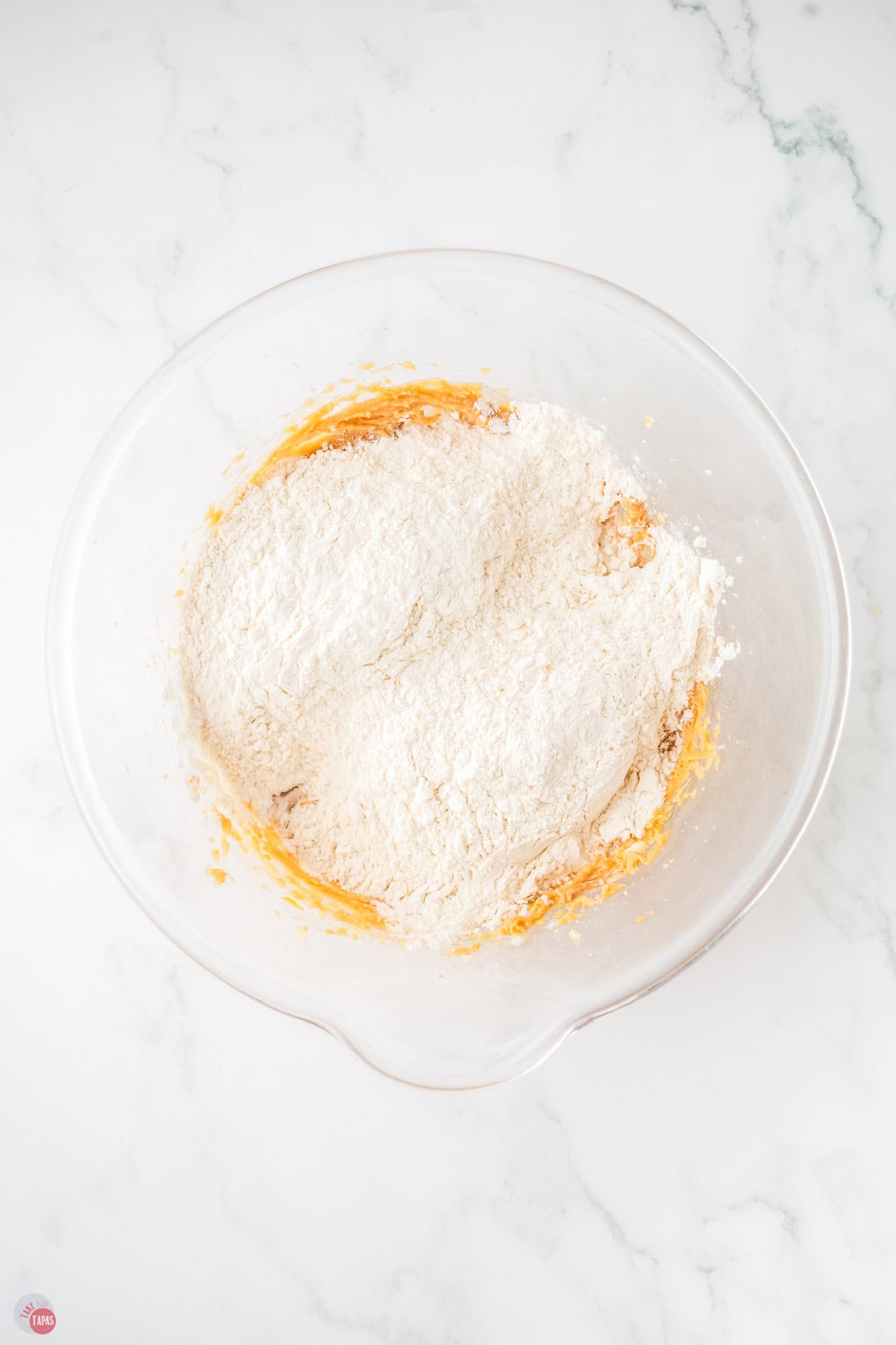 flour in a clear bowl with sugar in the bottor
