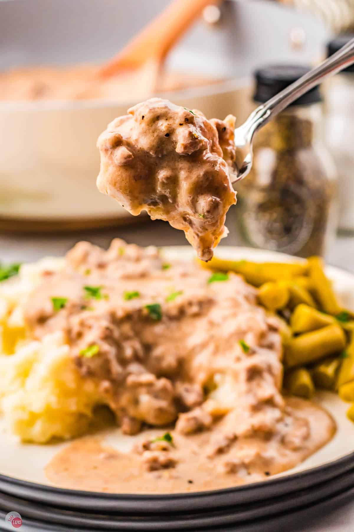 fork of mashed potatoes and gravy above a plate of green beans