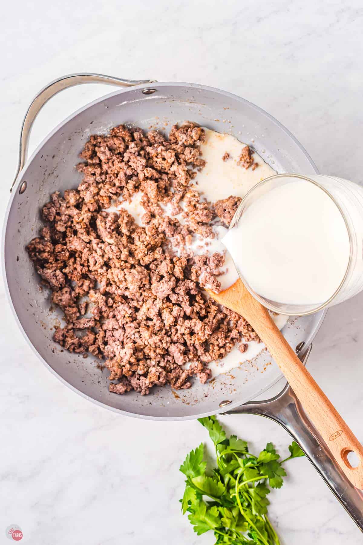 hand pouring milk into a skillet with ground beef