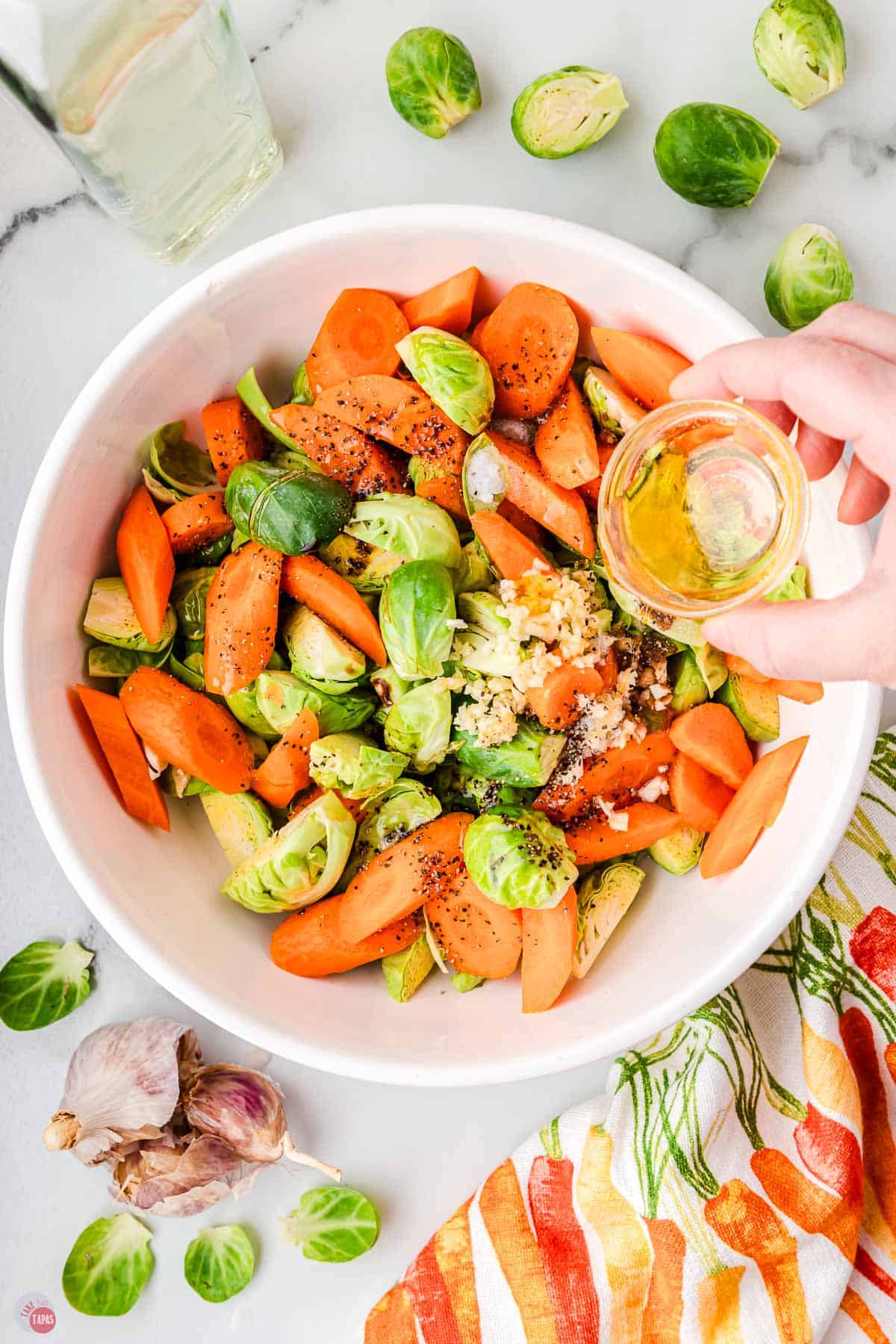 hand pouring olive oil and  spices over sprouts and carrots