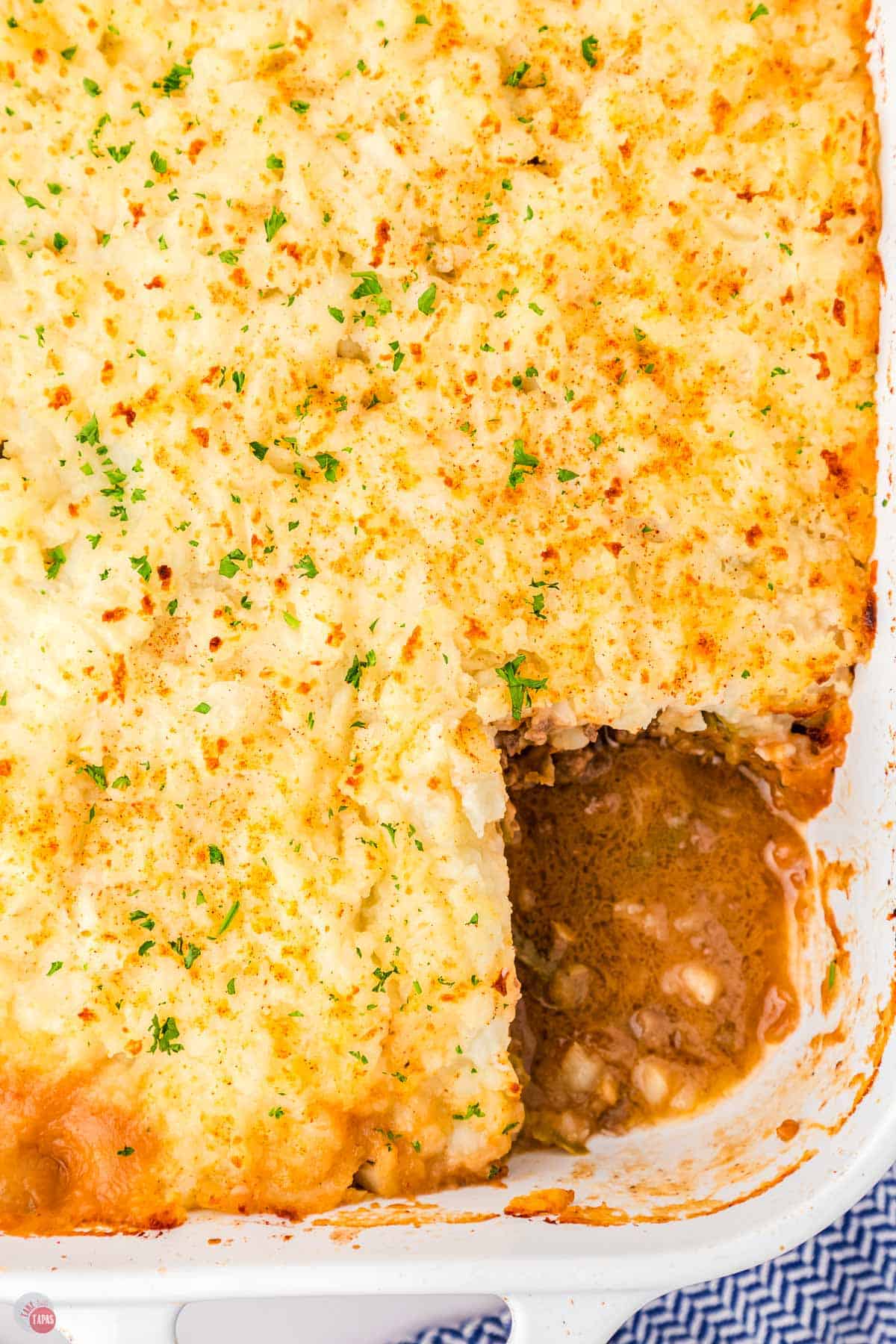 casserole topped with chopped parsley in a white dish with a square portion missing
