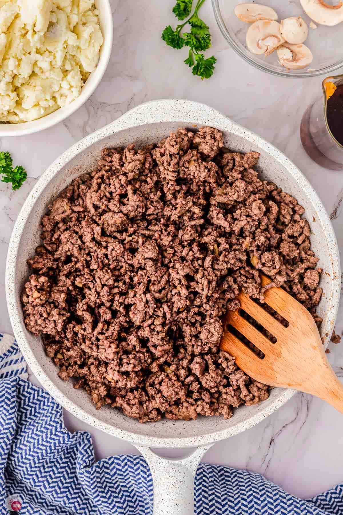 cooked ground beef in a white skillet with a wood spoon