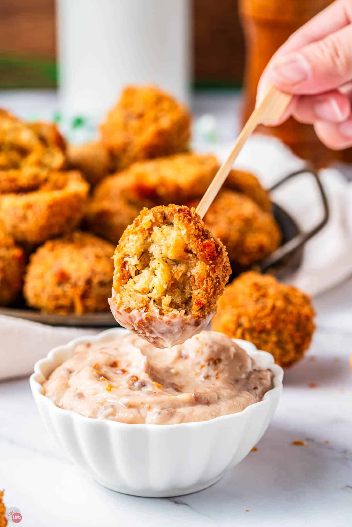 hand holding a dressing ball on a toothpick dipping it in cranberry dip