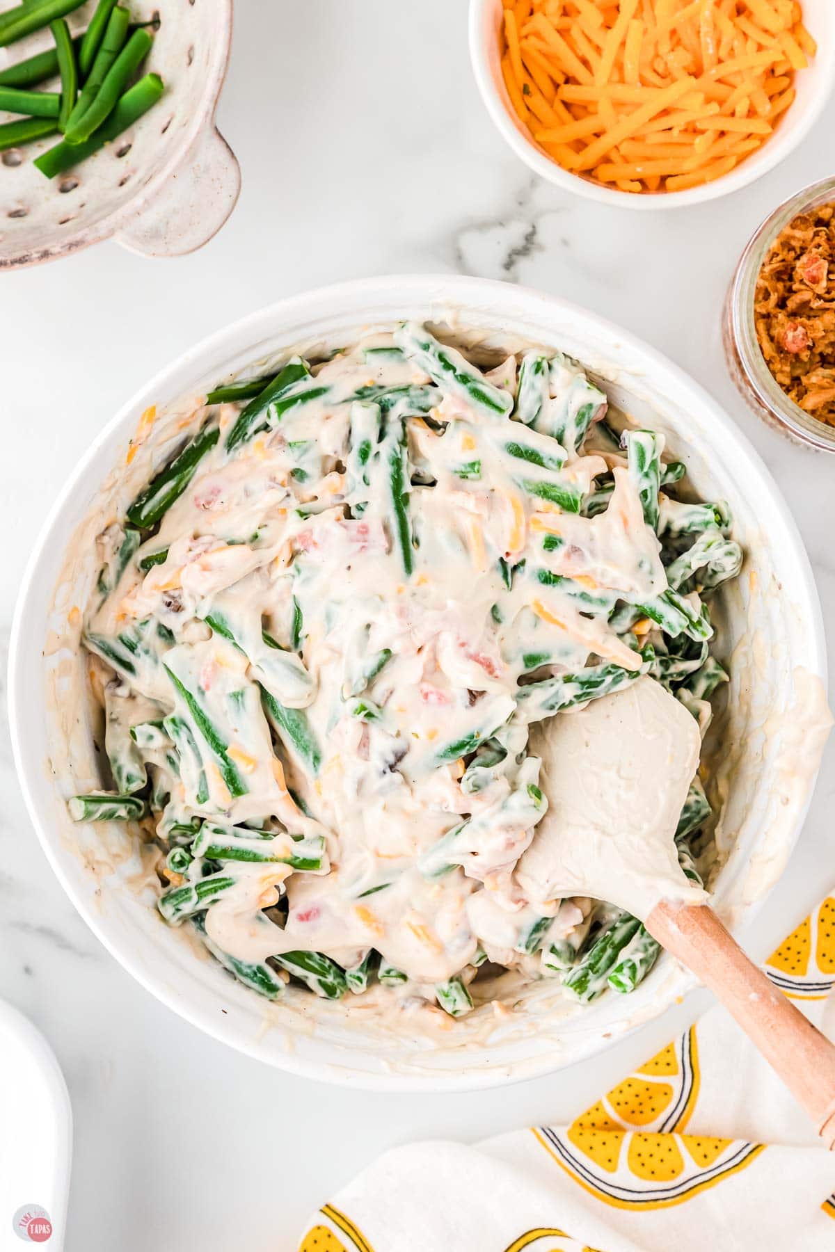 green beans in a white bowl with soup mixture on top and a spatula
