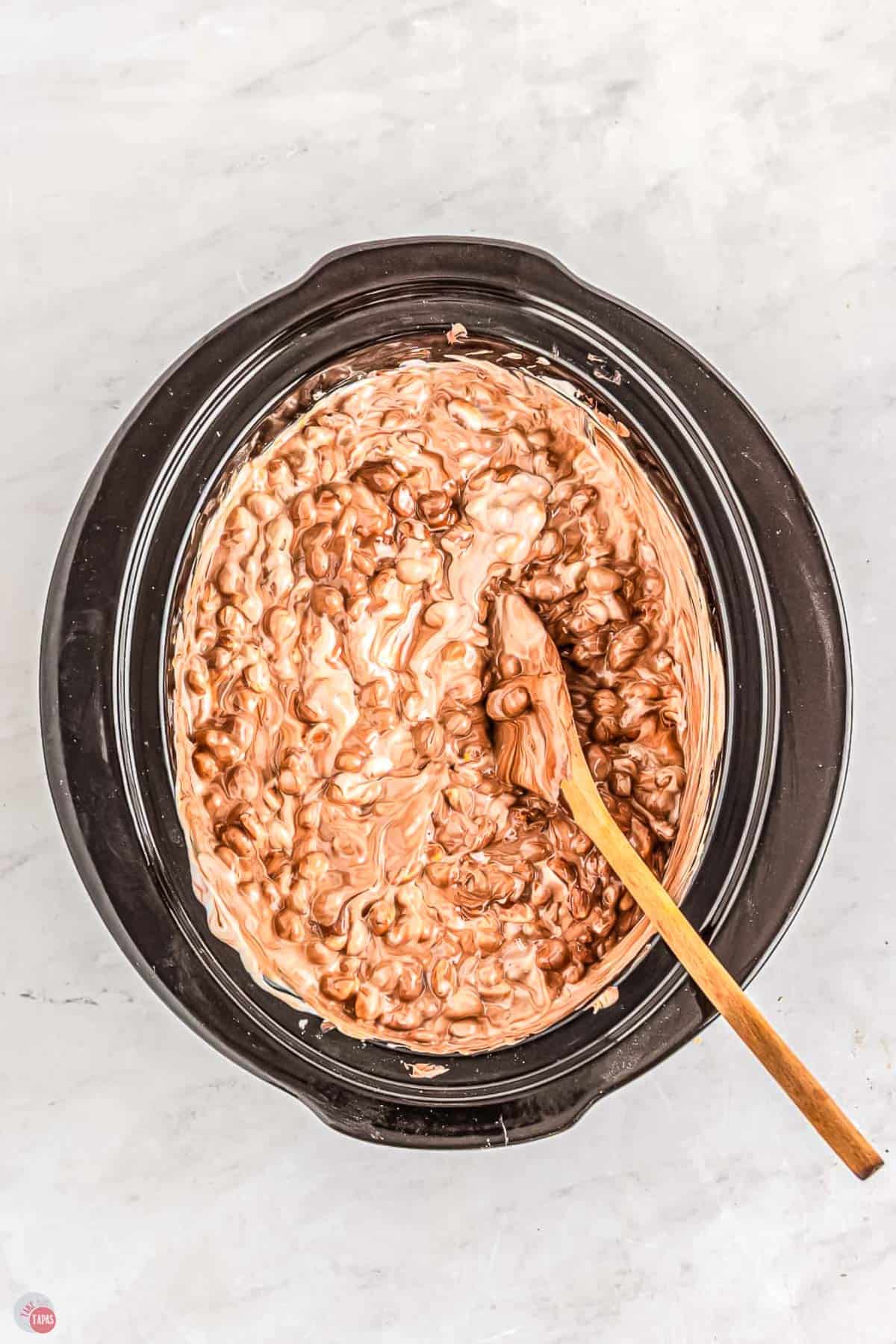 wood spoon stirring chocolate in a slow cooker pot