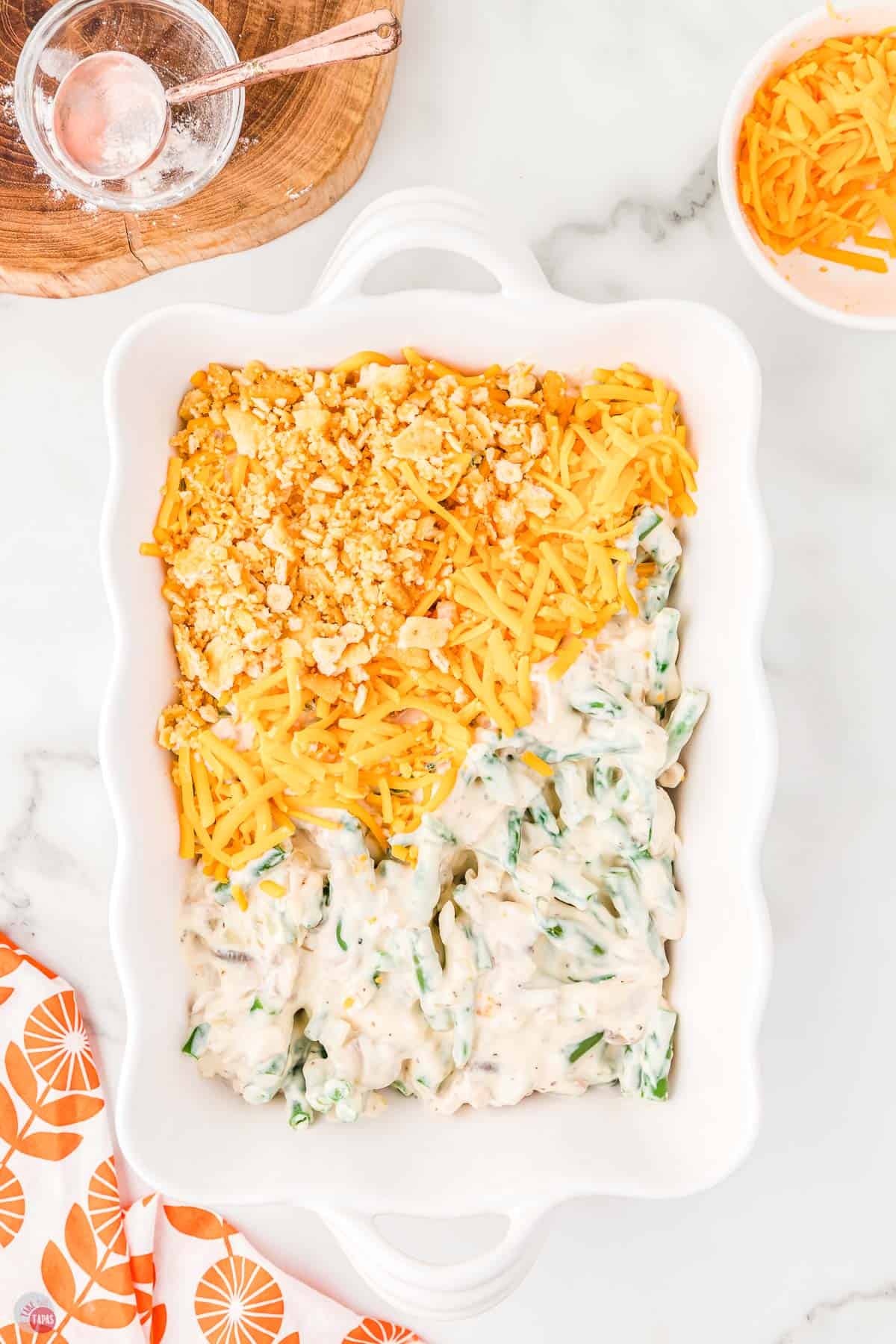 green bean casserole partially covered with cheese and cracker crumbs