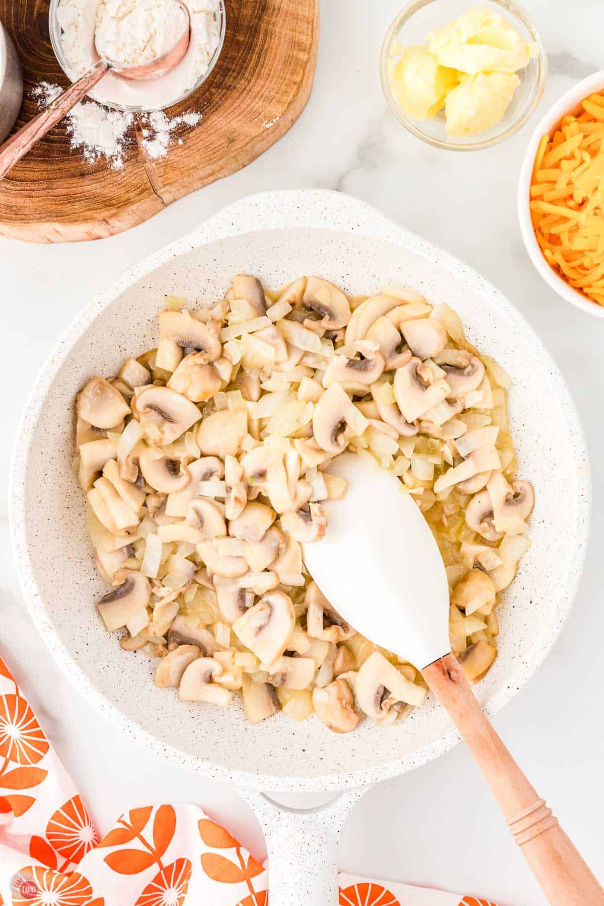 mushrooms and onions cooking a white pan with a spatula