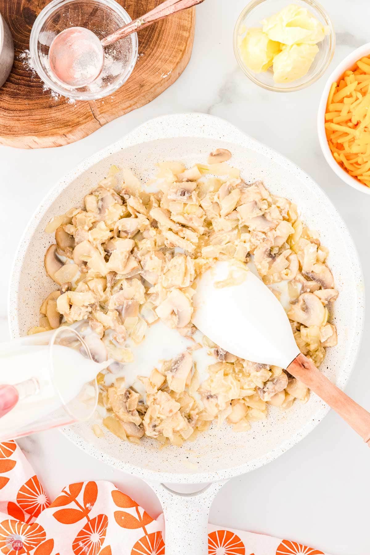 mushrooms and onions in a skillet with milk being poured in with a spatula