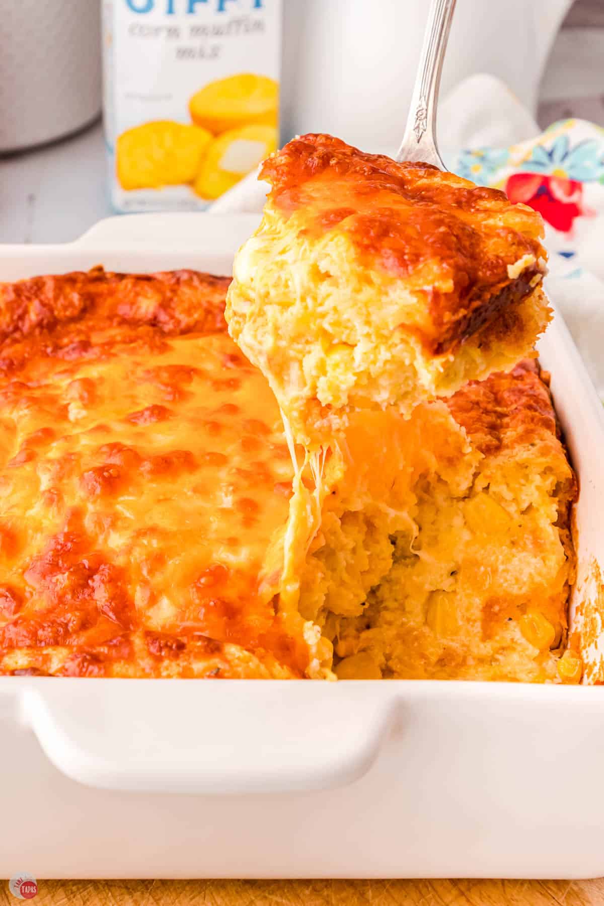 scoop of cheesy corn casserole above a white baking dish