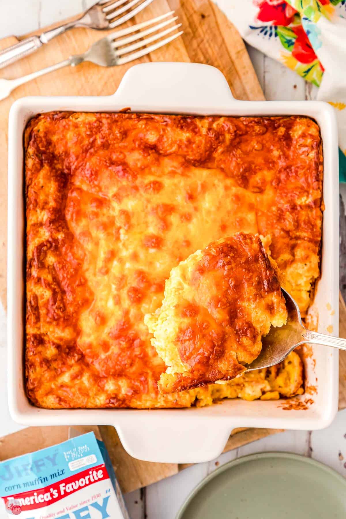 spoon scooping corn casserole out of a square white dish