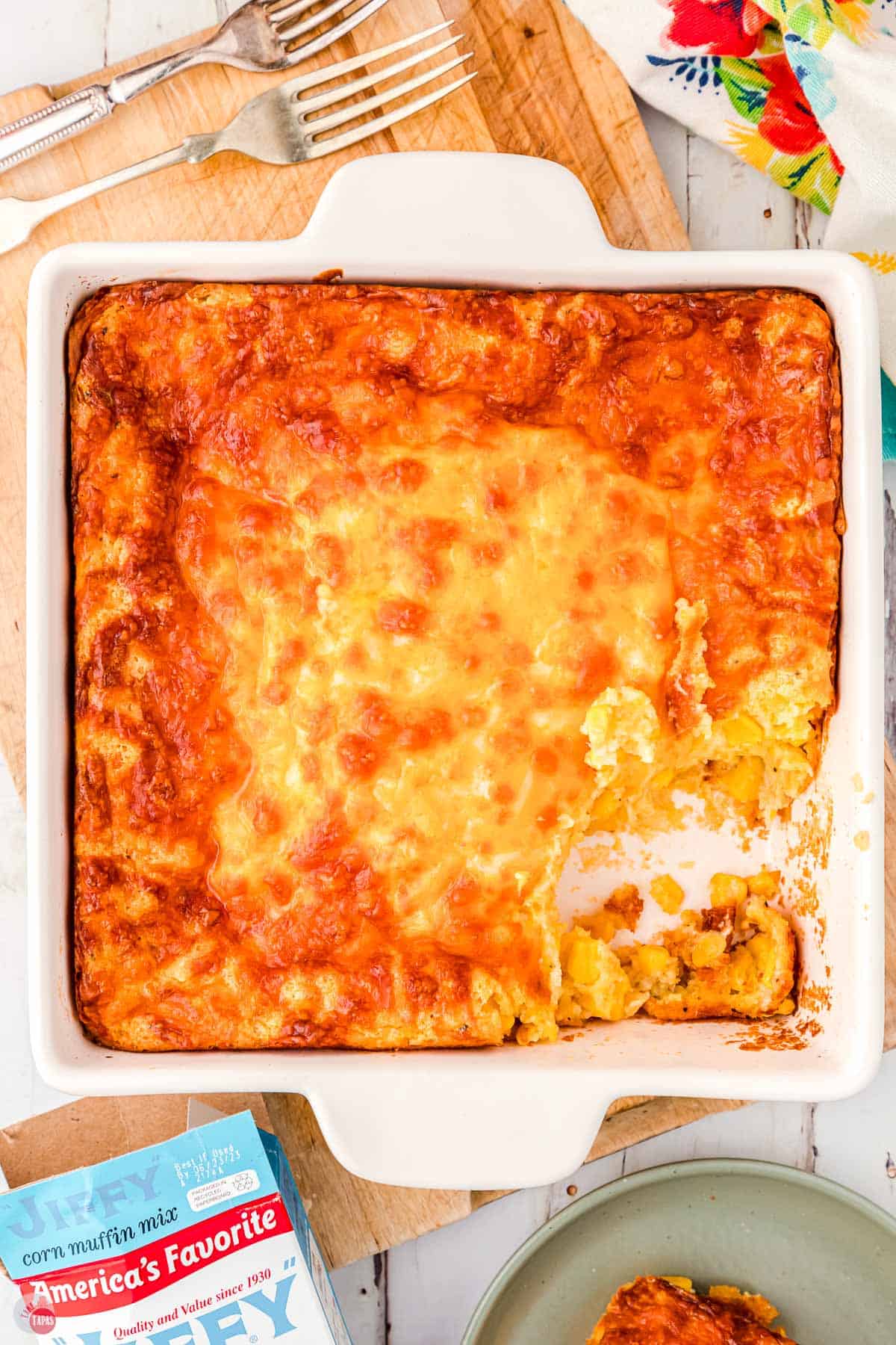 square white dish with corn casserole and a scoop missing