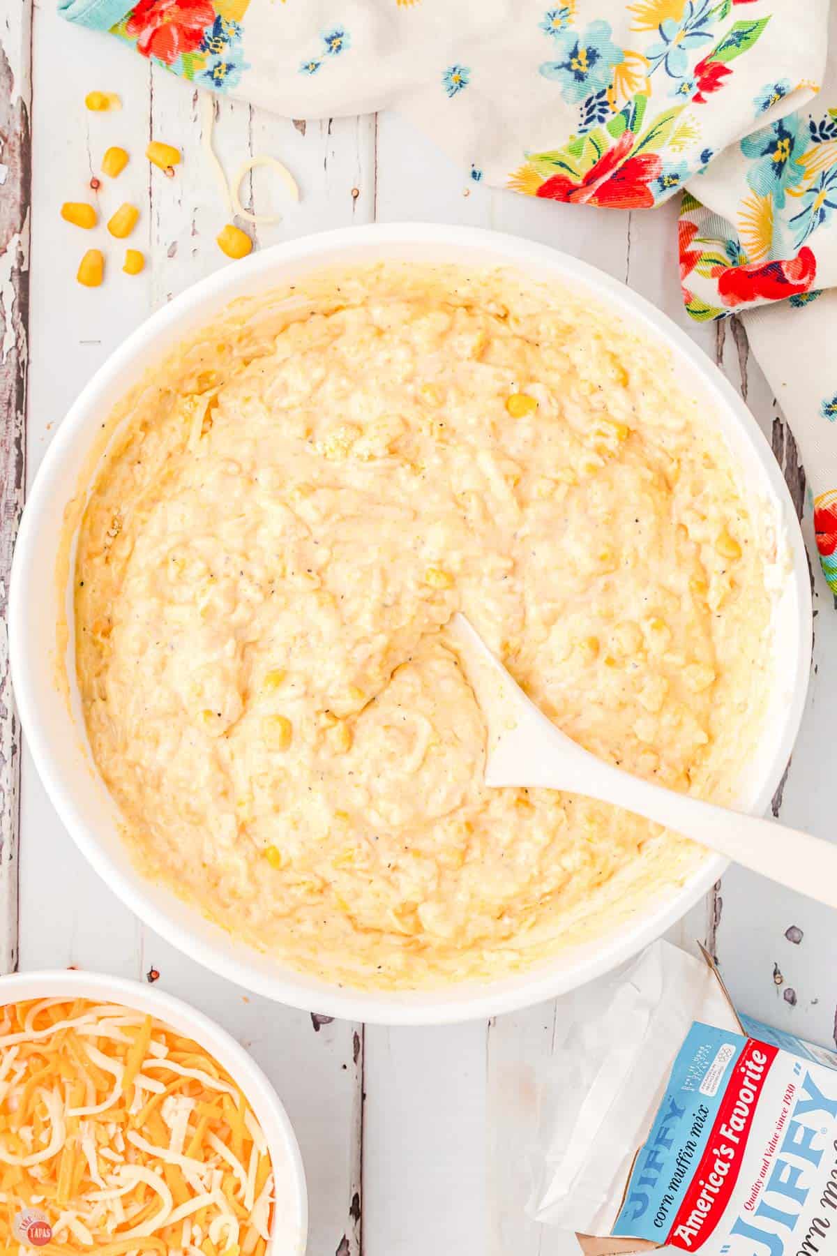 corn casserole batter in a white bowl being stirred with a spoon