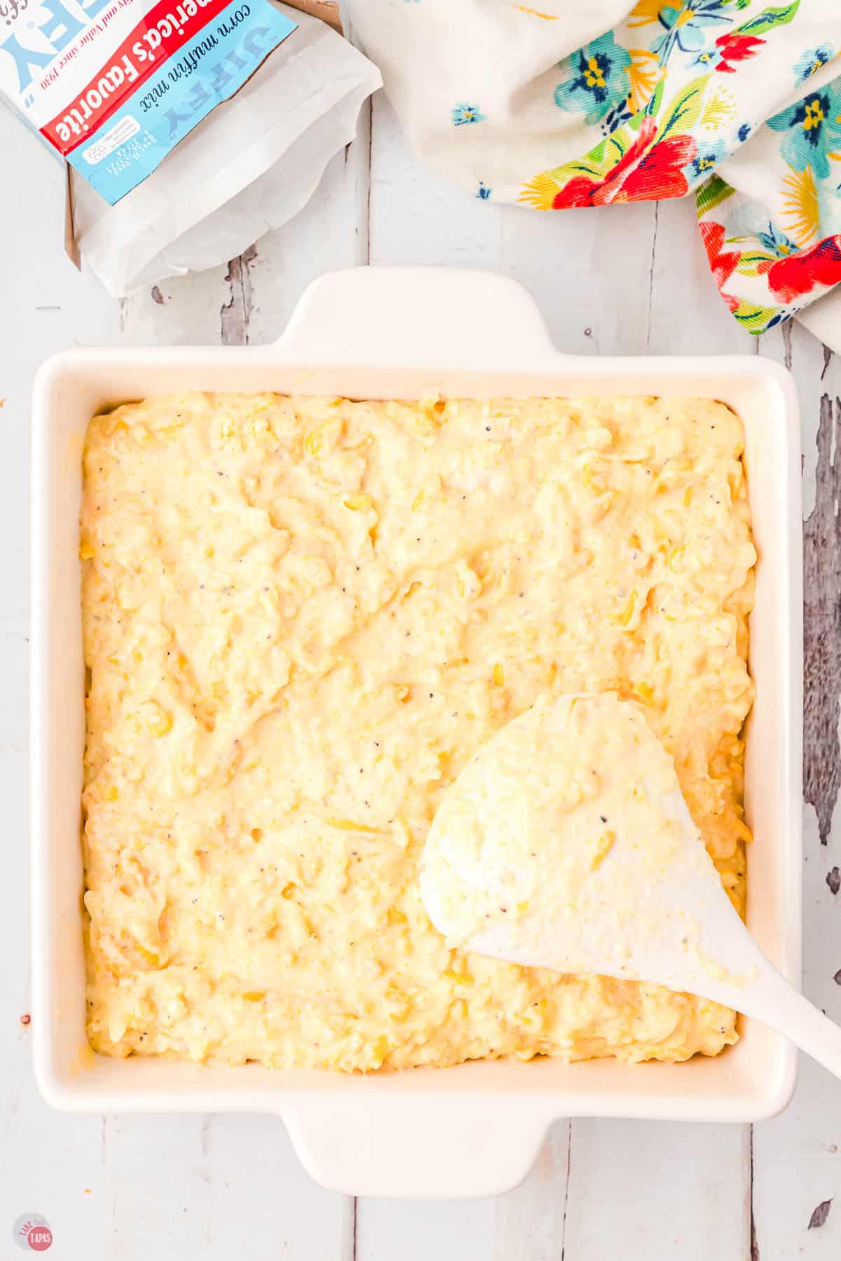 corn casserole in a square white dish with a spoon in it