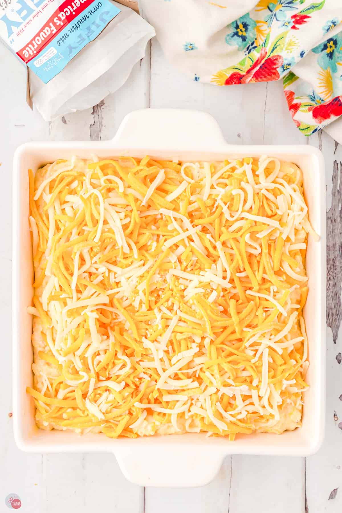 shredded cheese on top of an unbaked casserole in a square white dish