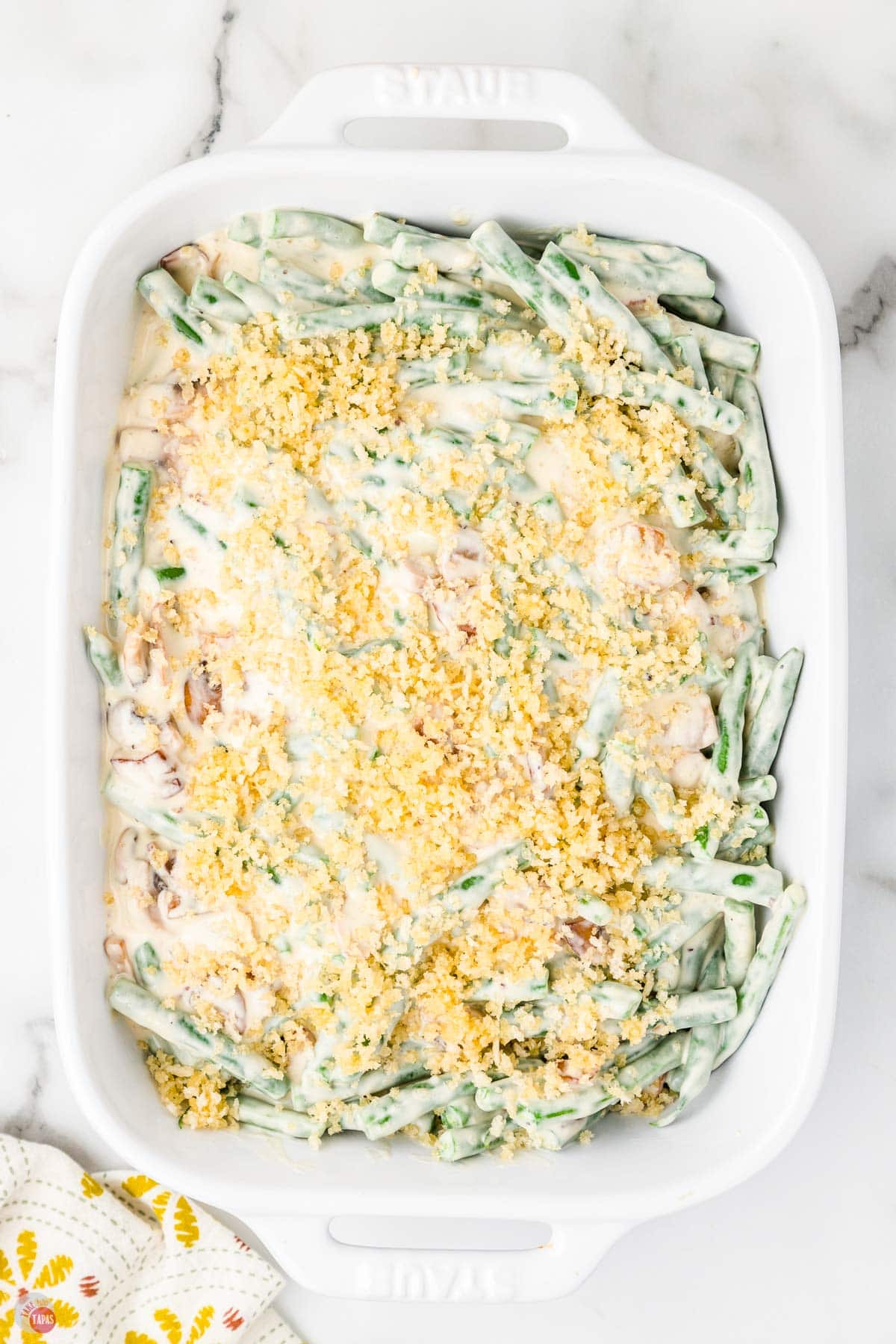 Creamy green bean casserole with crispy fried onions and melted cheese in a white baking dish.