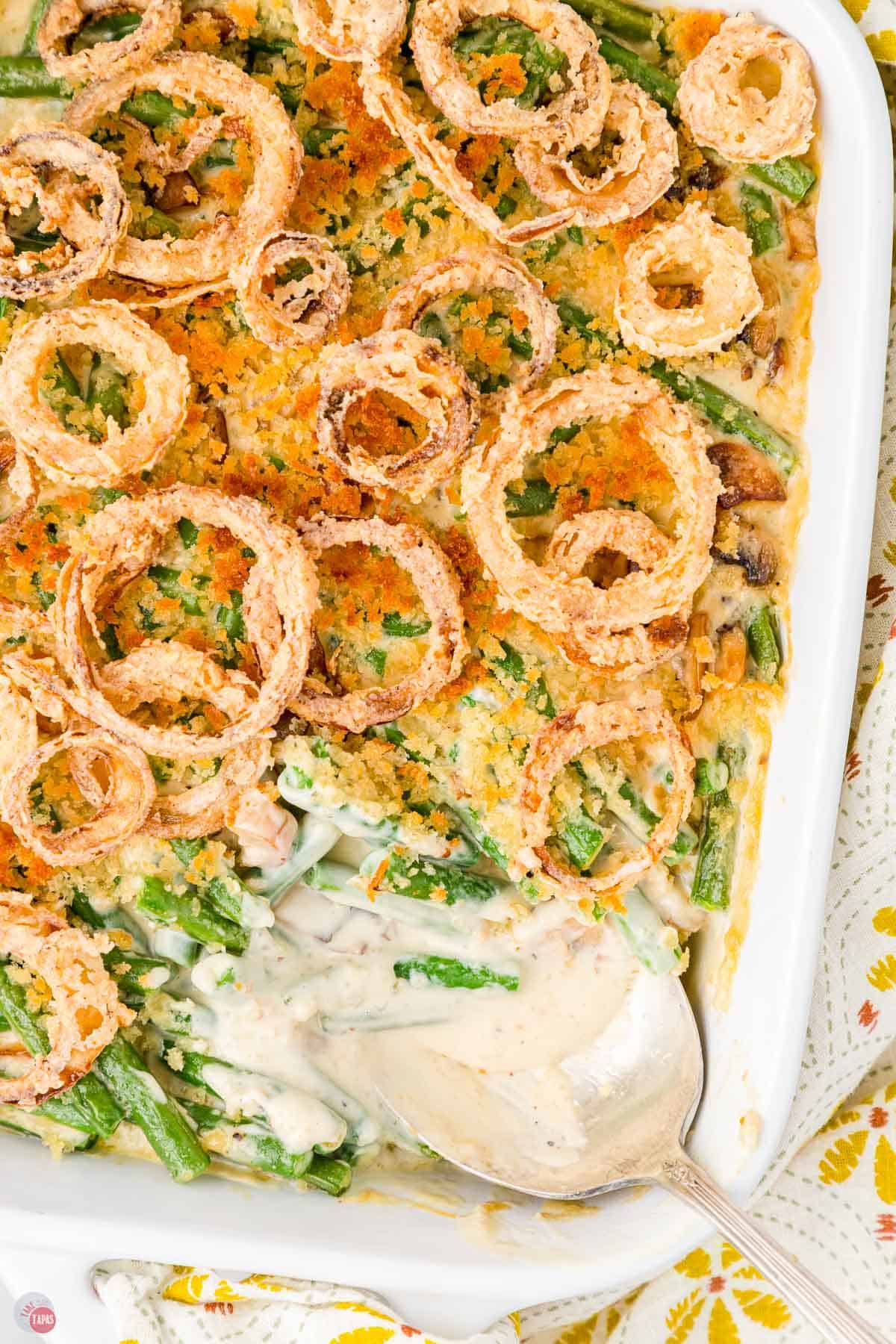 Joanna Gaines green bean casserole topped with onion rings with a metal spoon taking a scoop out