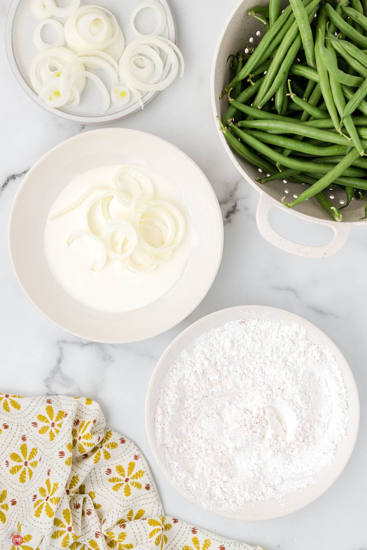 onion rings in a bowl of milk next to a bowl of flour