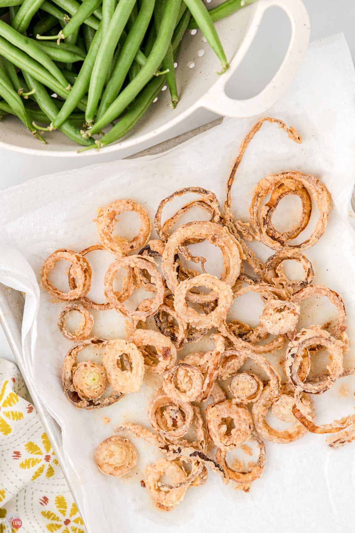 fried onion rings on a paper towel next to w bowl of green beans