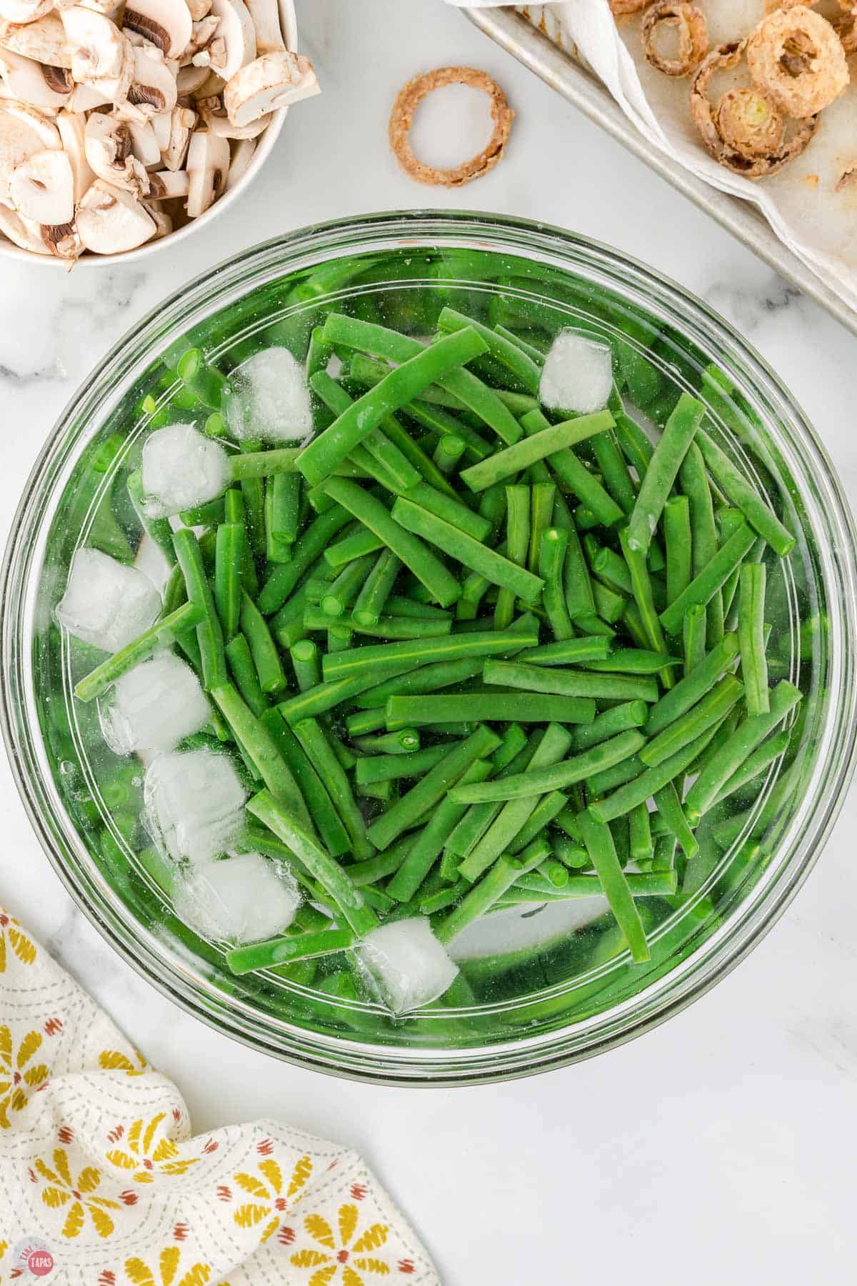 fresh cooked green beans in a metal bowl with water and ice cubes