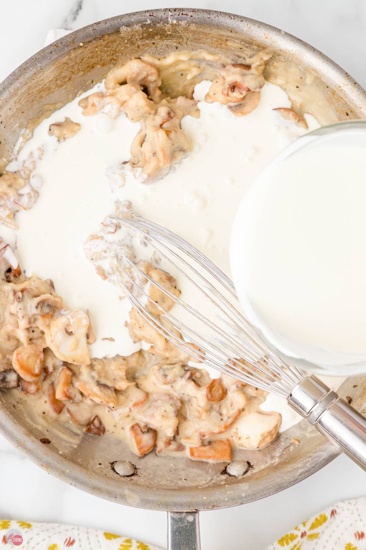 milk being poured into a skillet of cooked mushrooms