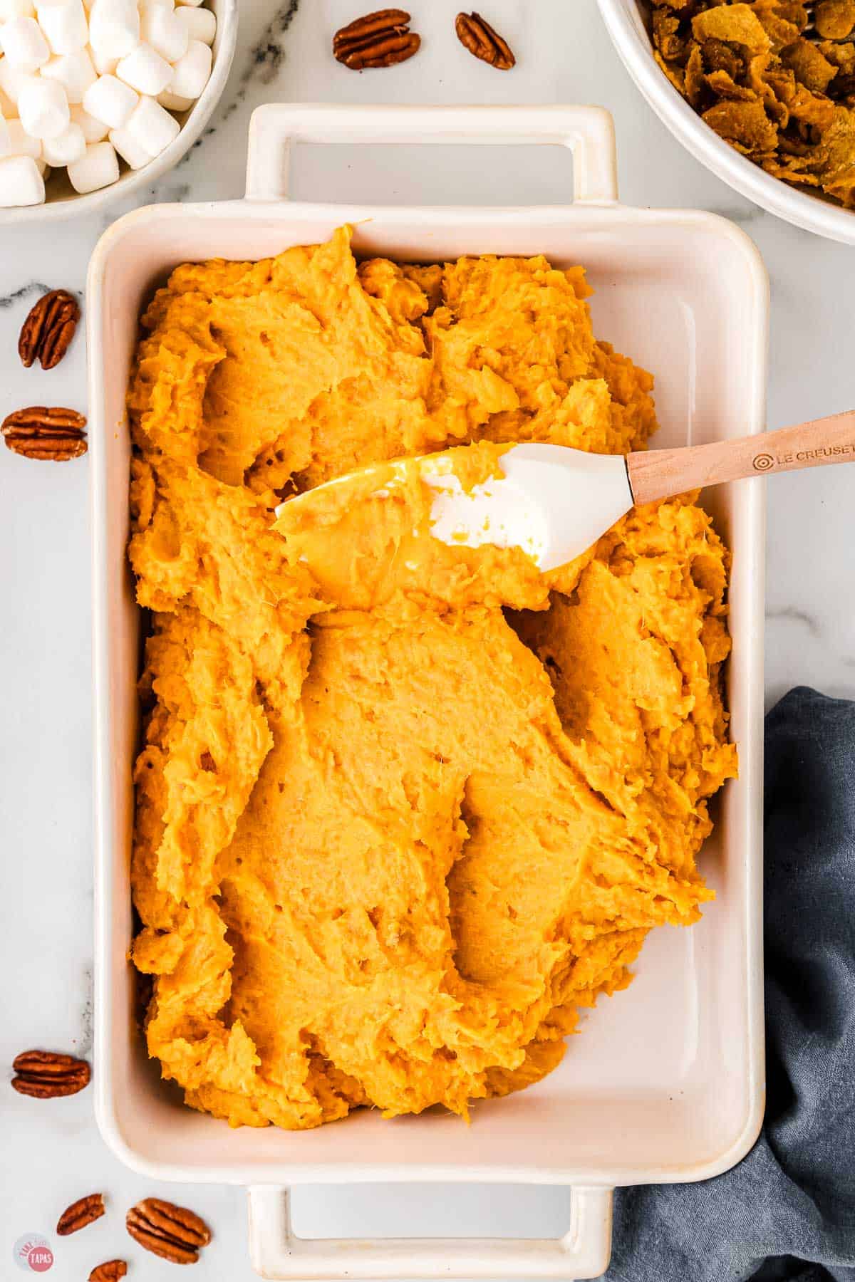 spatula spreading mashed sweet potatoes in a white casserole dish