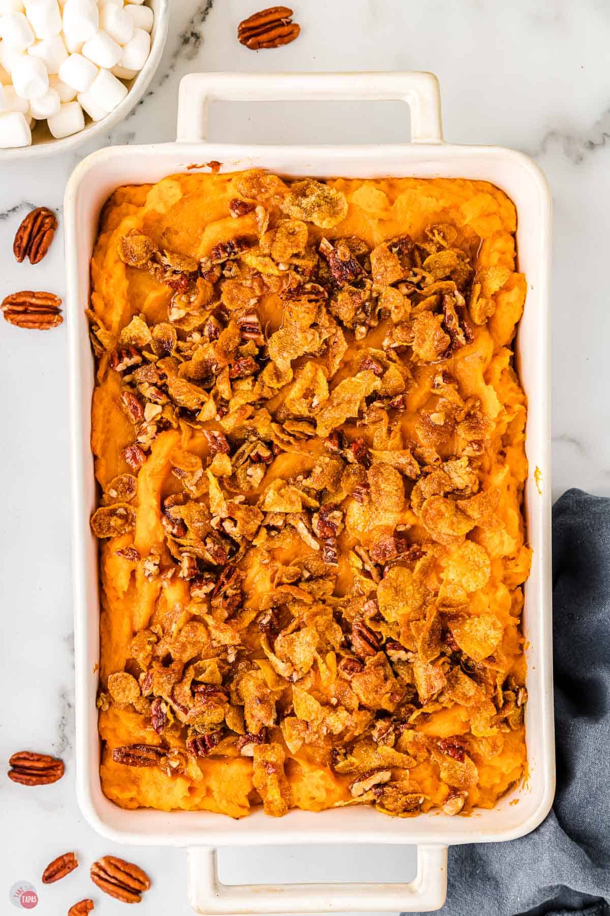 unbaked sweet potato casserole in a white dish topped with pecans and cornflakes