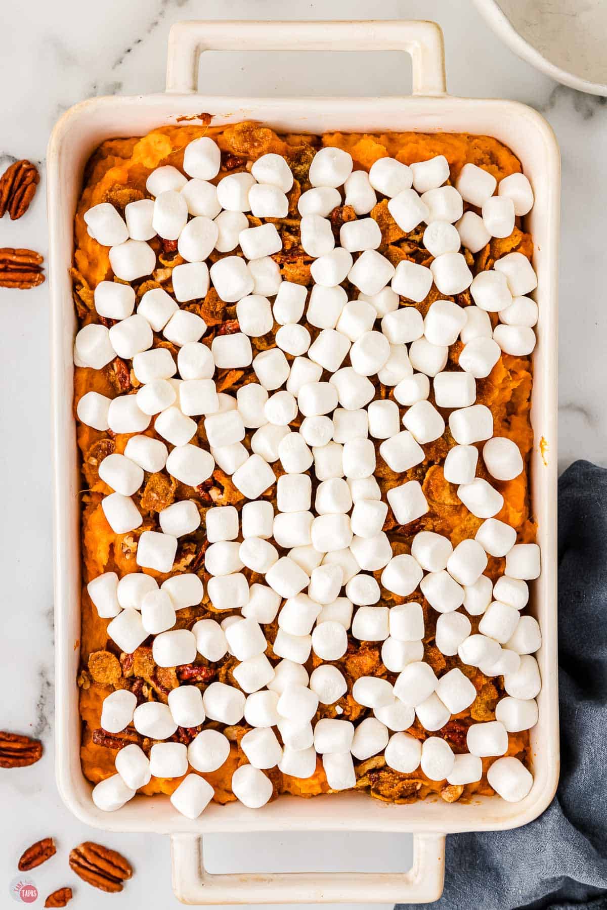 marshmallows on top of a layer of sweet potatoes in a white dish.