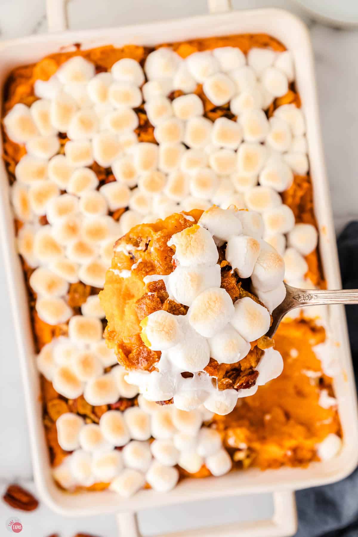 overhead picture of scoop of sweet potato casserole over a white casserole dish