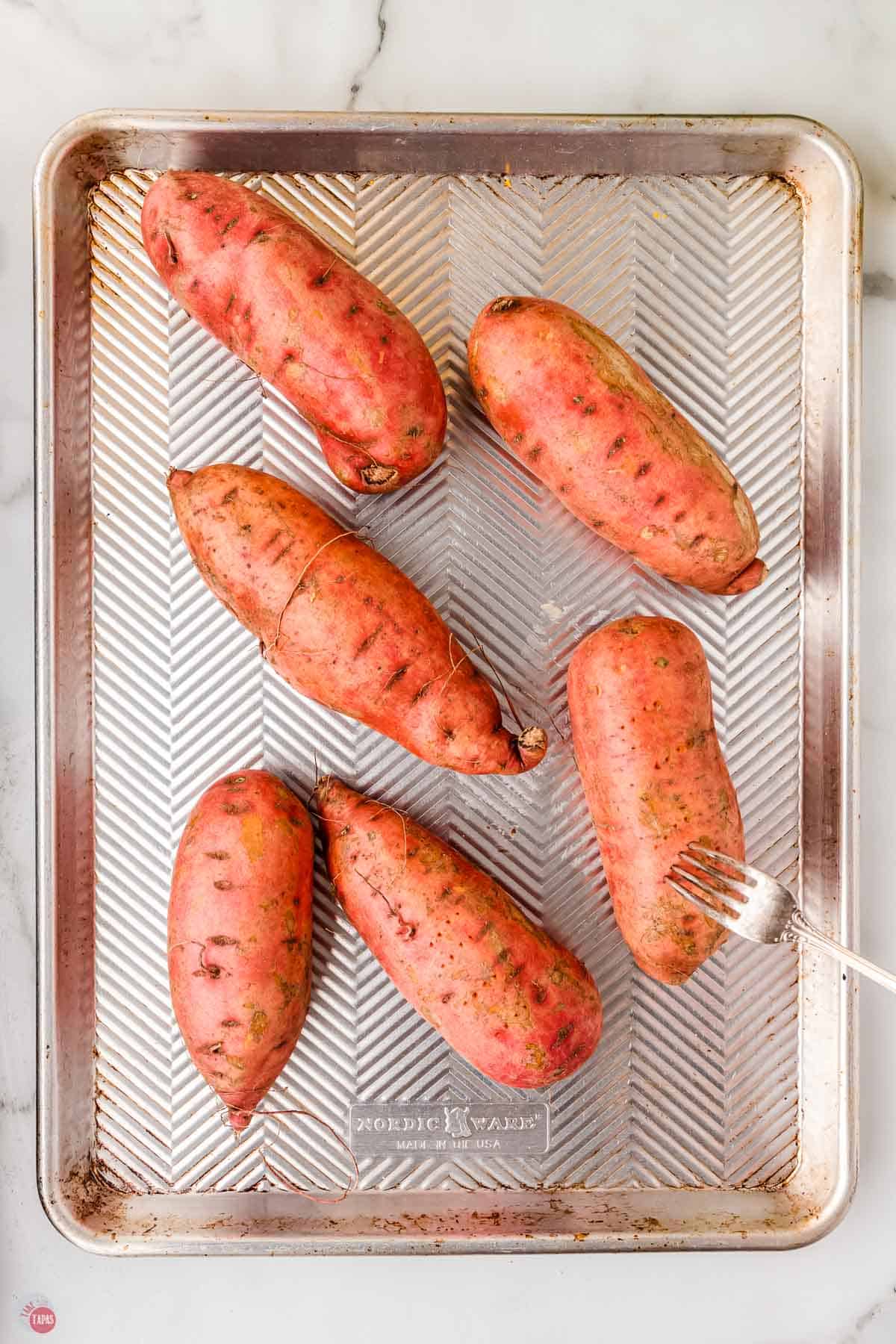 sweet potatoes on a baking sheet with a fork poking one