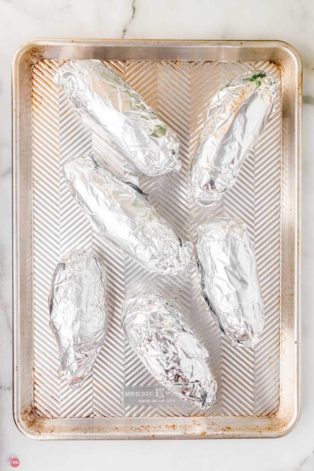 6 sweet potatoes wrapped in aluminum foil on a baking sheet