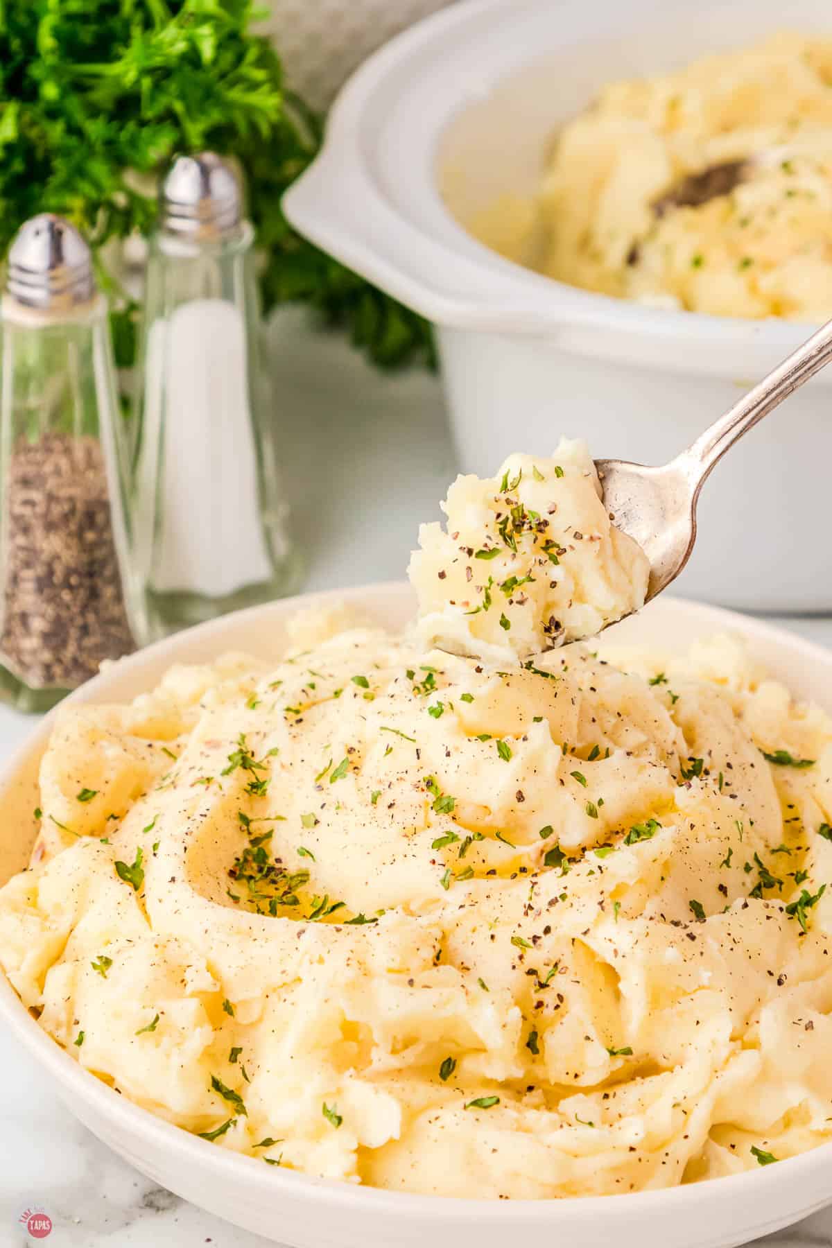 white bowl of million dollar mashed potatoes with a spoon in it