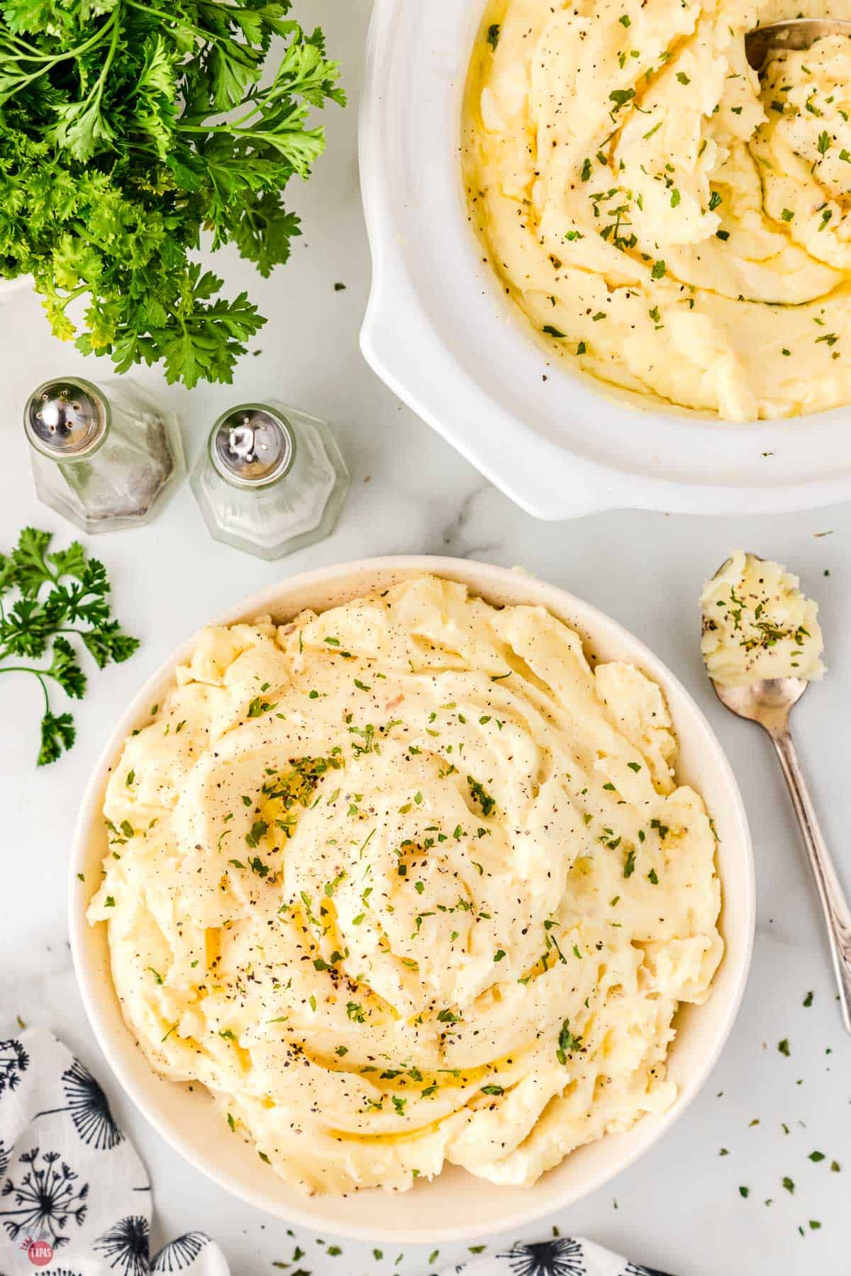 two bowls of million dollar mashed potatoes next to salt and pepper shakers