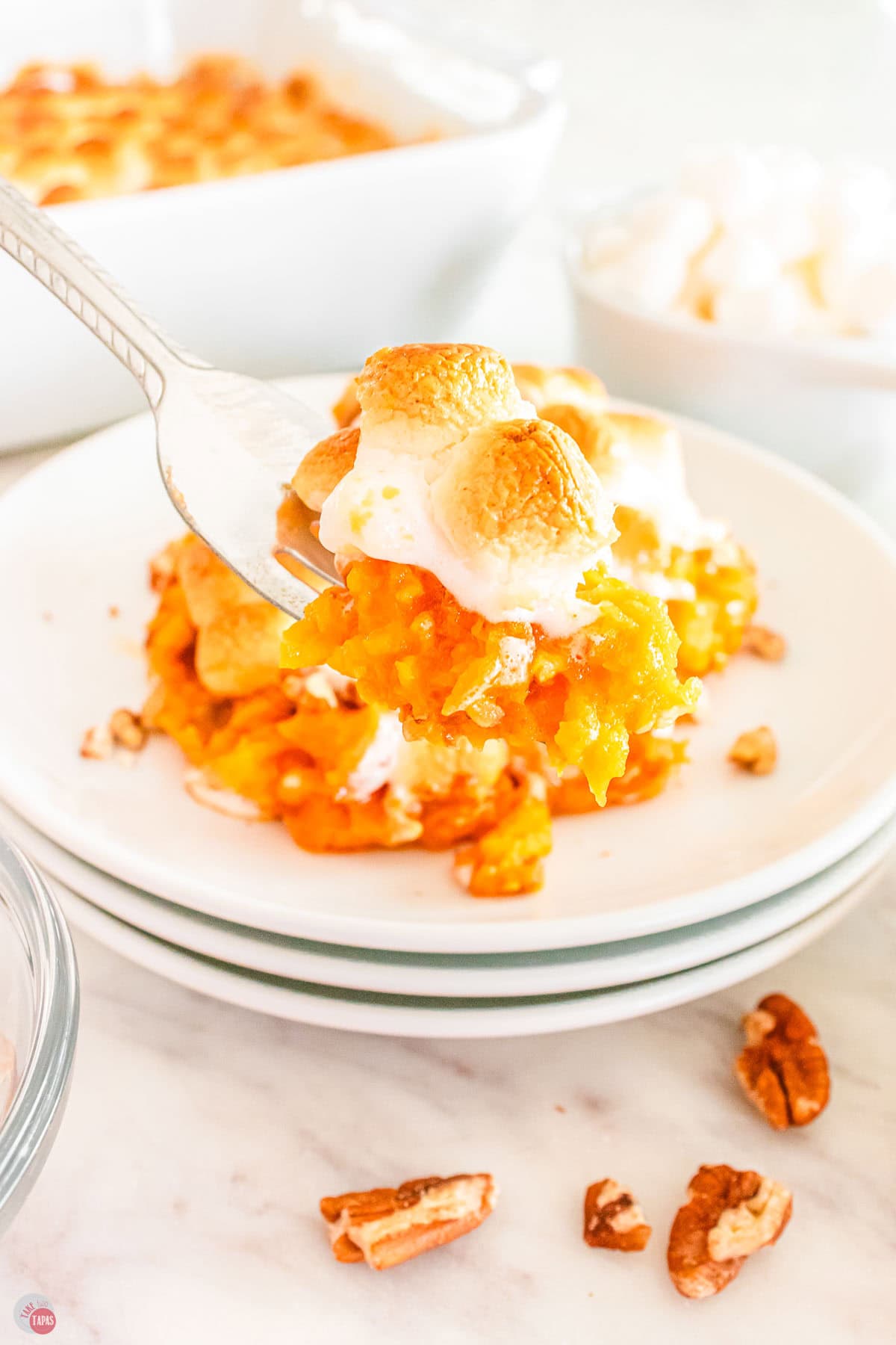 fork with bite of sweet potatoes and marshmallows in front of a stack of white plates