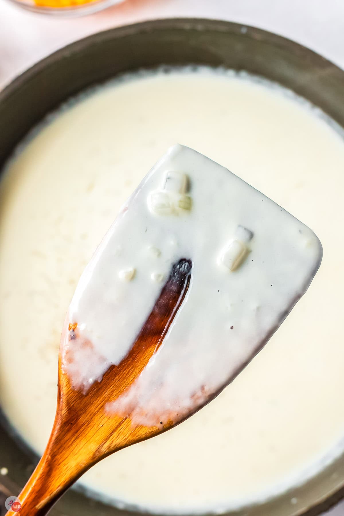 close up of cream sauce on a wood spoon with a finger swipe missing out of it
