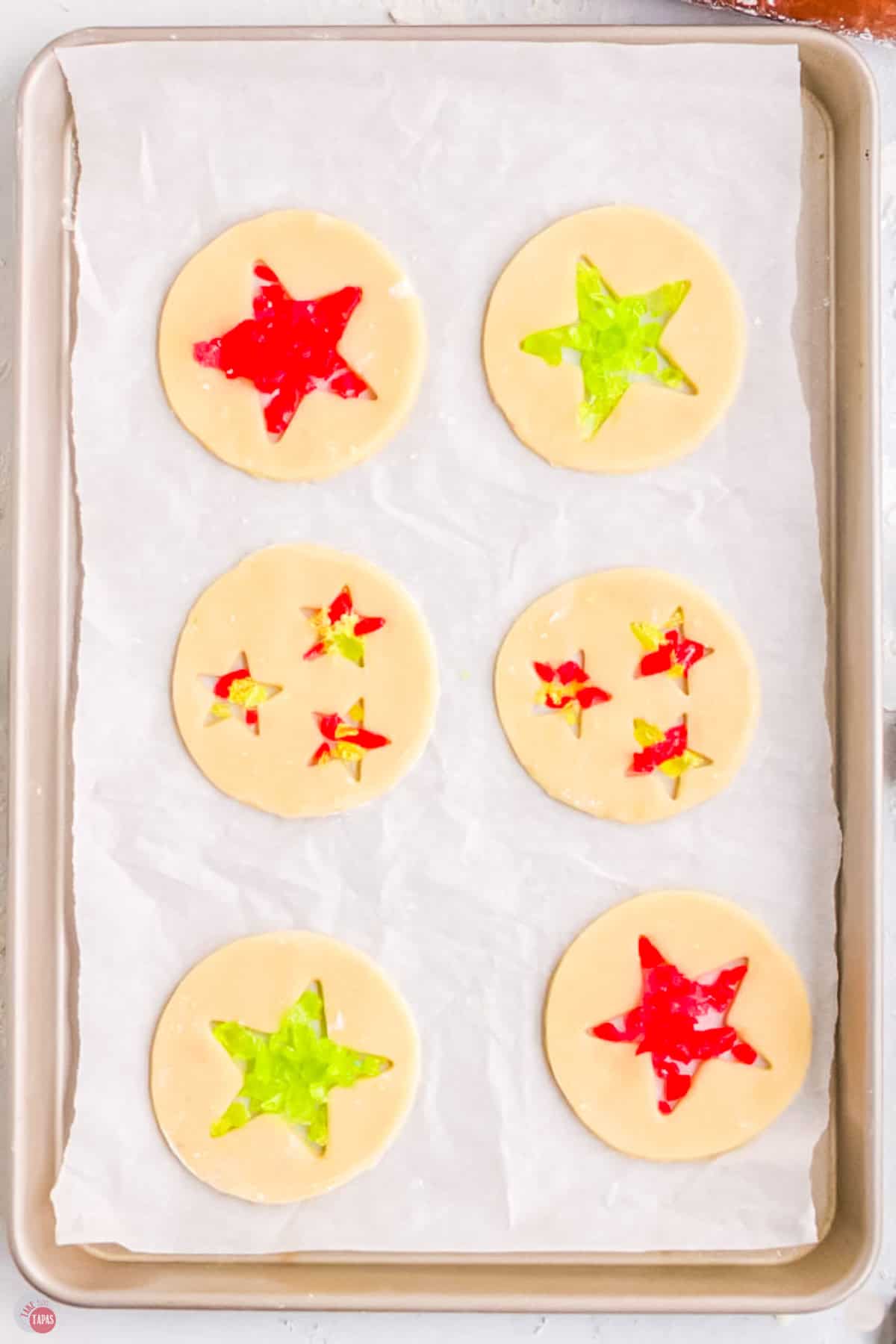 sugar cookies on a baking sheet with star shapes cut out and filled with crushed candy