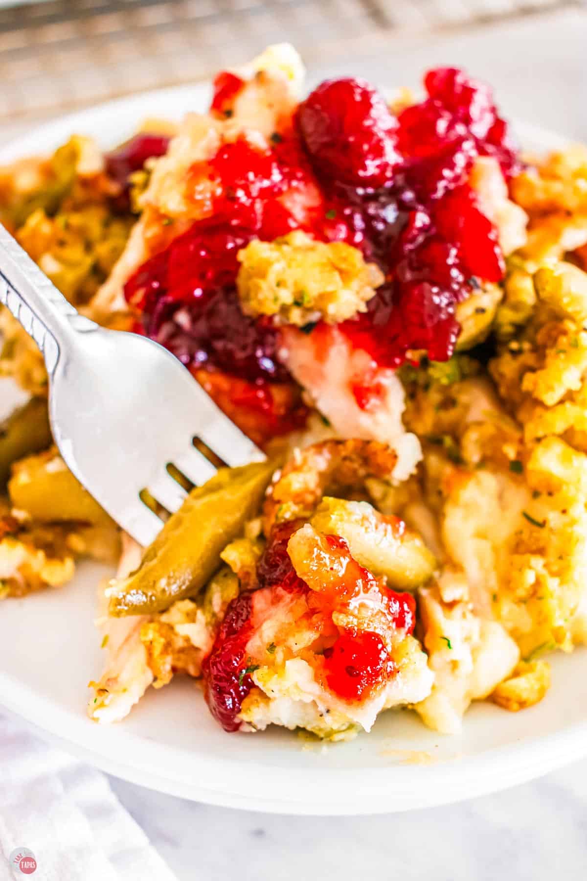 fork with bite of mashed potatoes with green beans and cranberry sauce