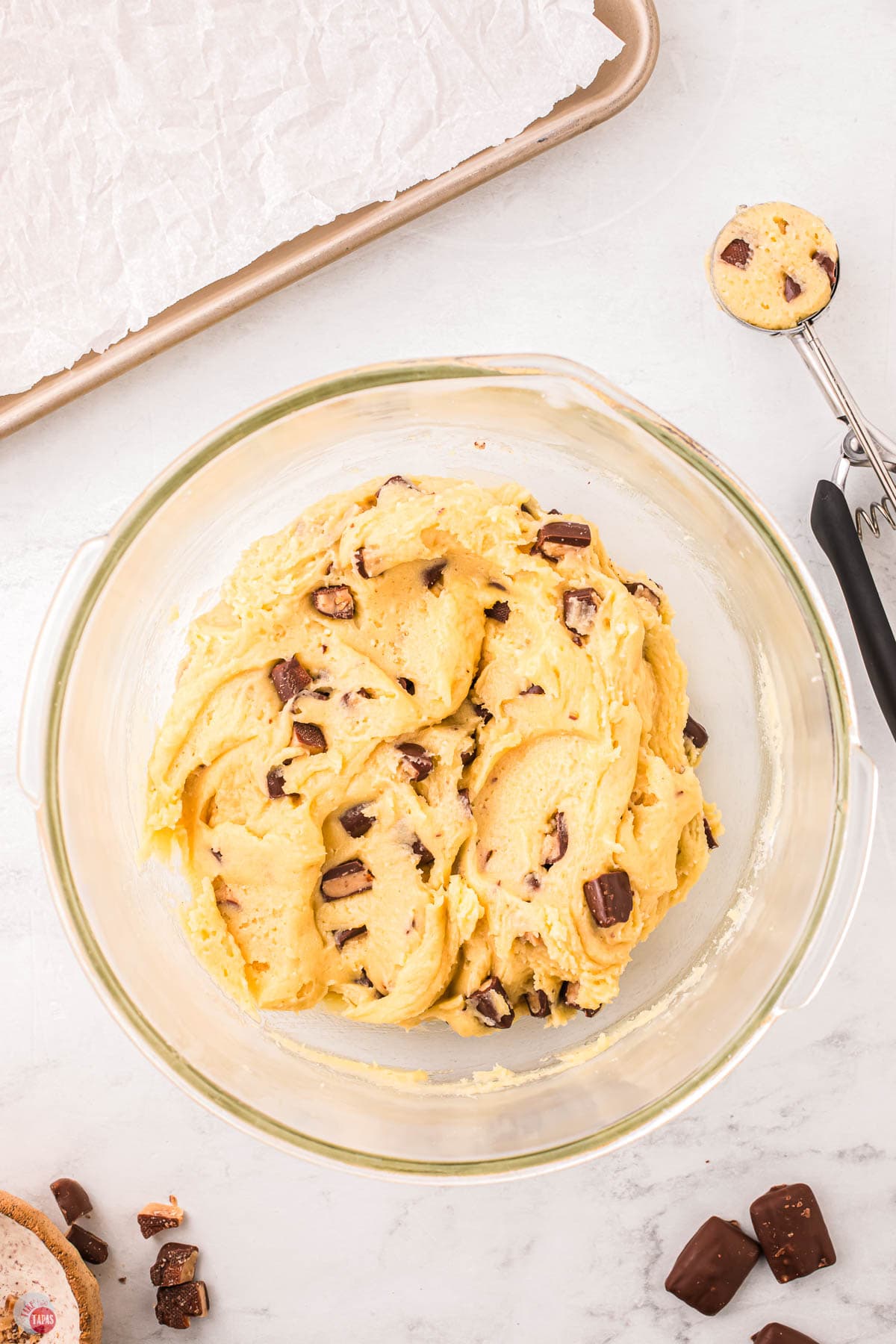 cookie dough in a clear bowl next to a baking sheet