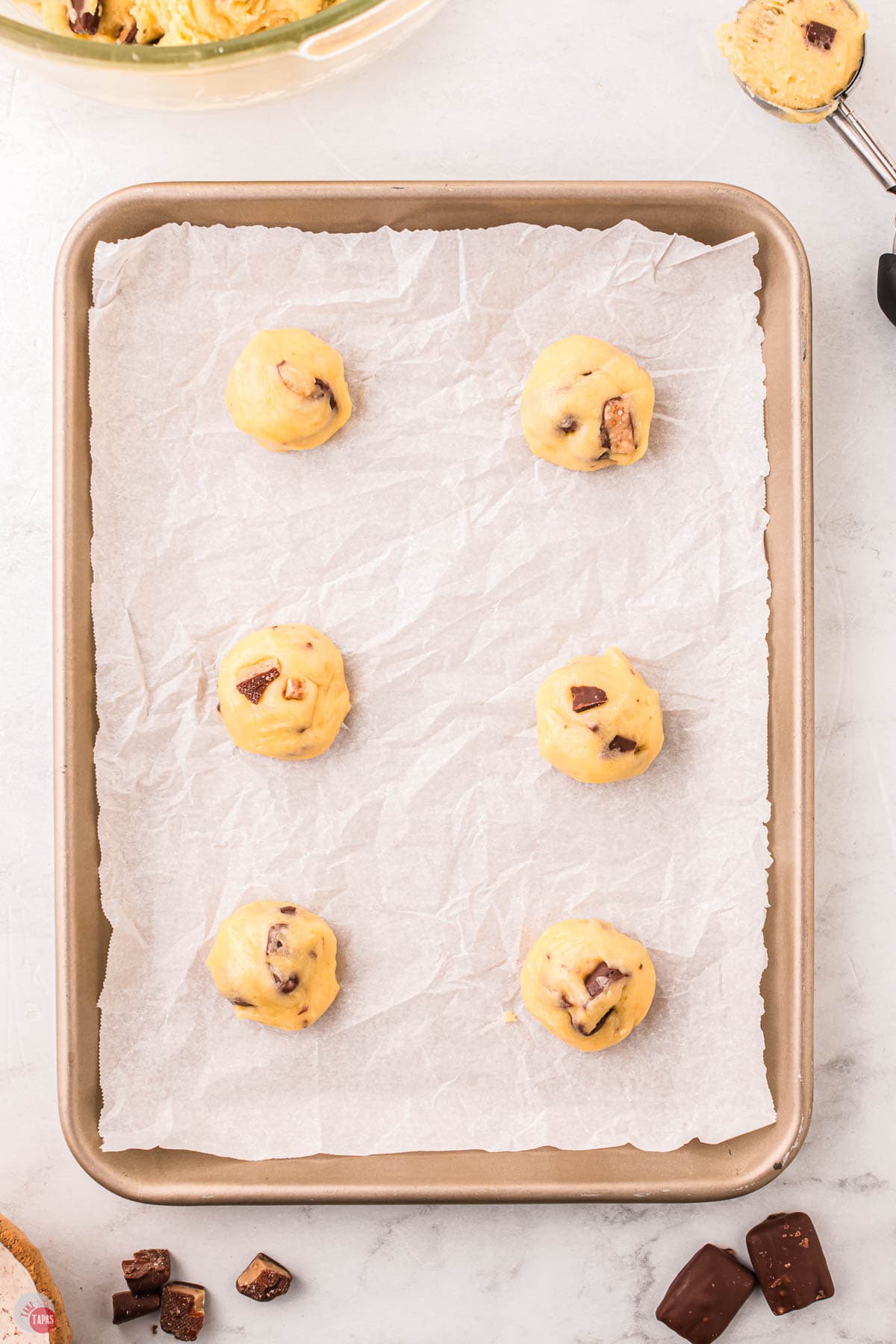 parchment paper lined baking sheet with balls of raw cookie dough on it