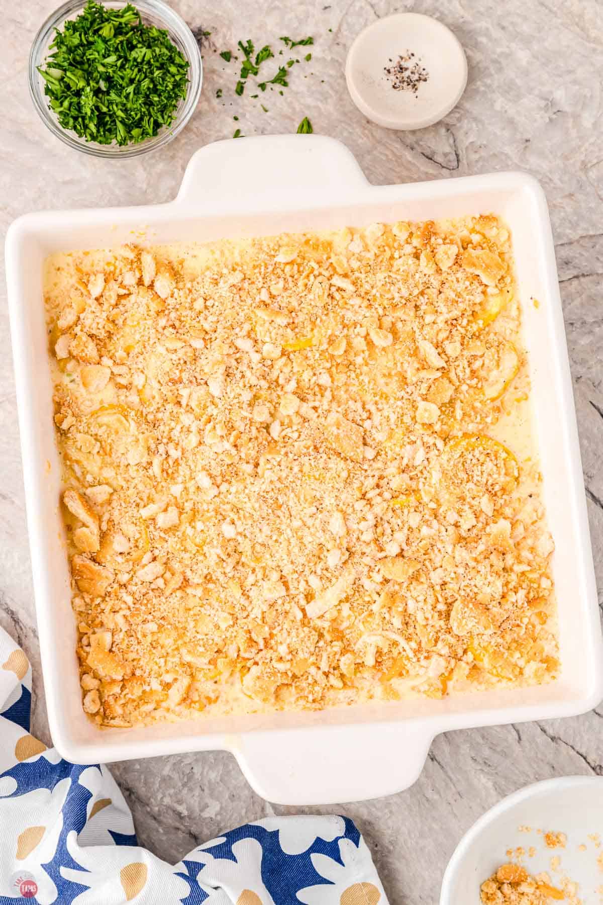 unbaked squash casserole in a white dish with crushed crackers on top 