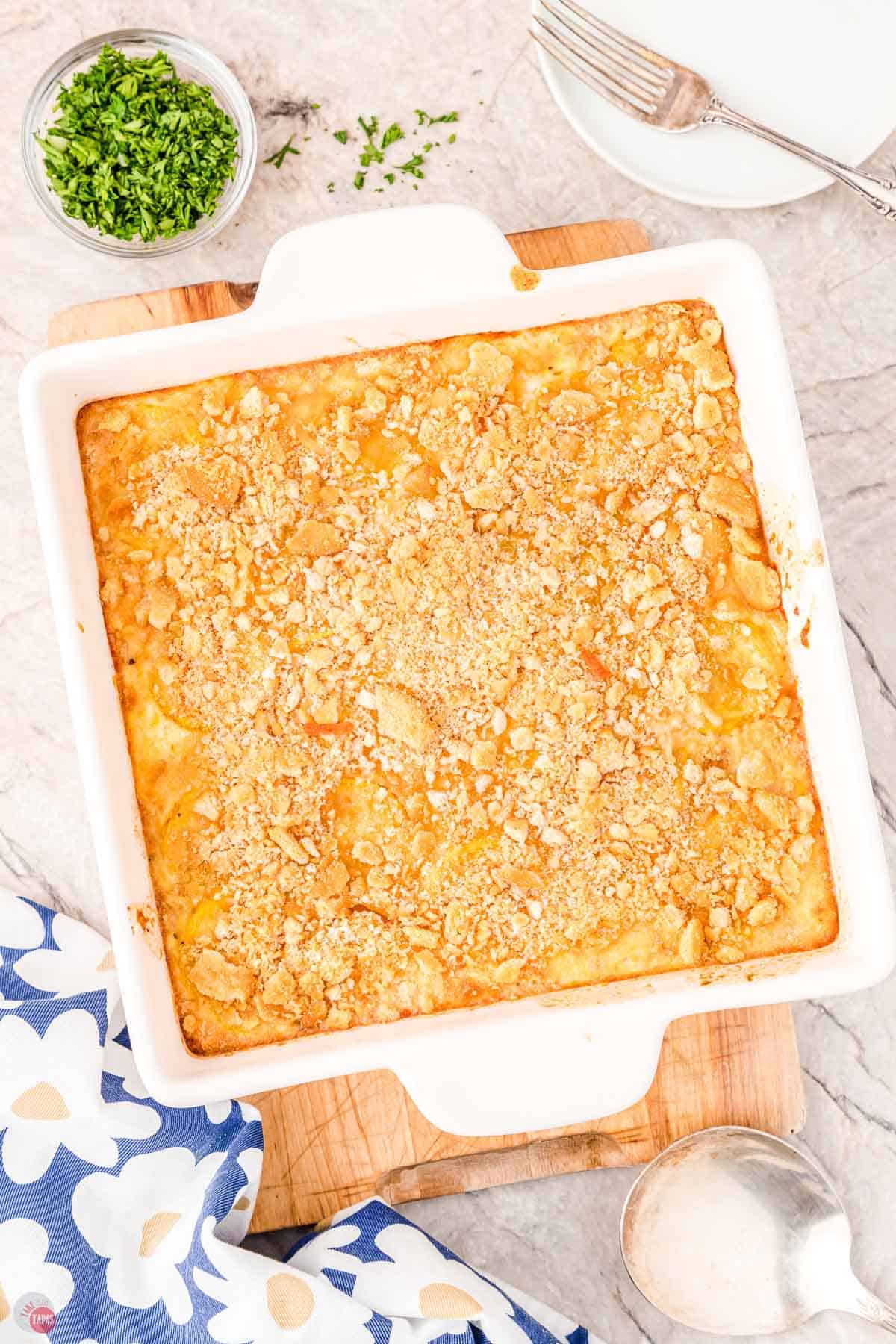 baked casserole in a square white dish with a bowl of chopped parsley