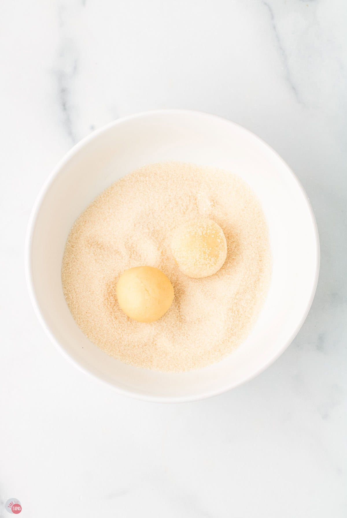 two balls of cookie dough in a bowl of sugar
