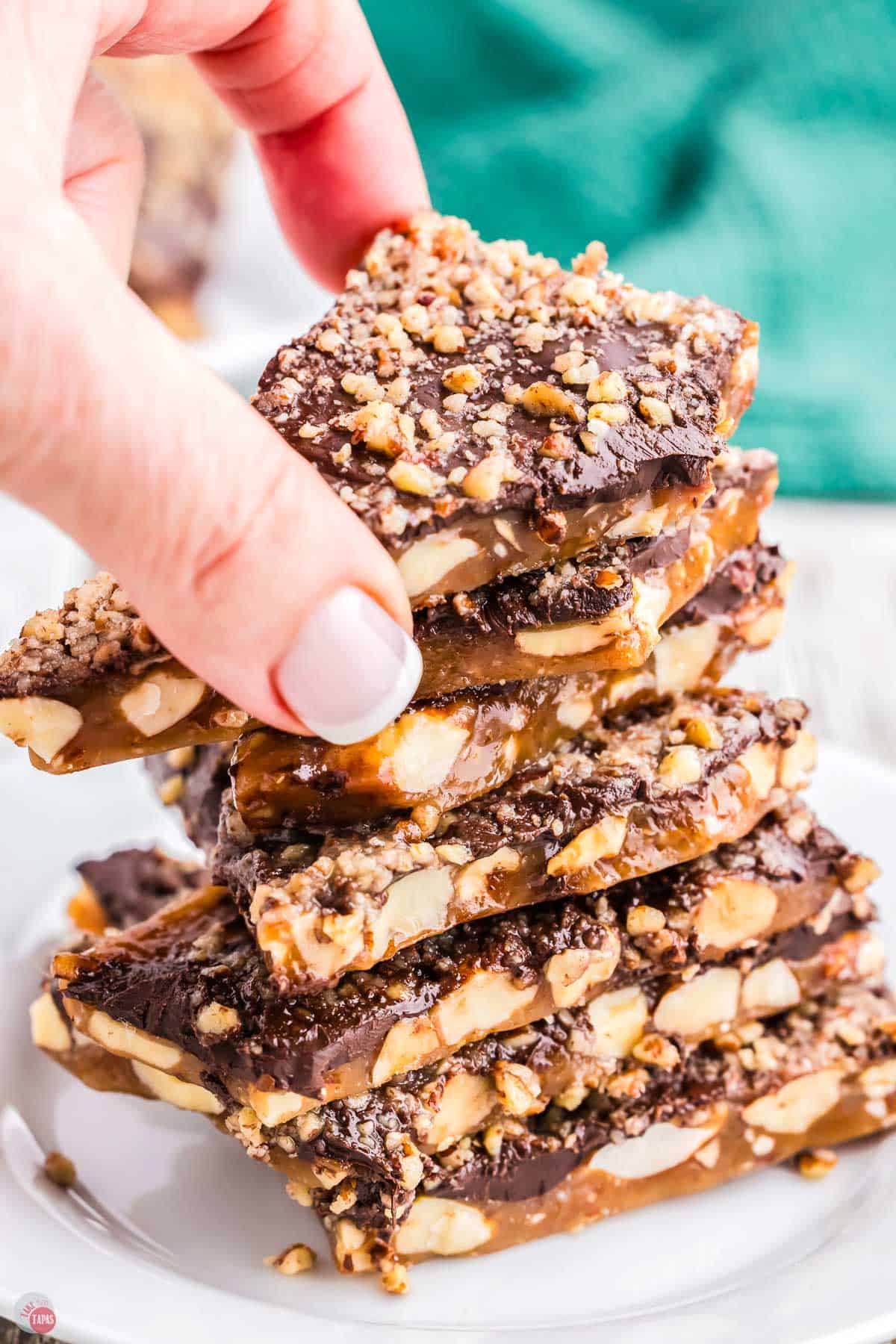 hand picking up a piece of almond roca candy off the top of a stack