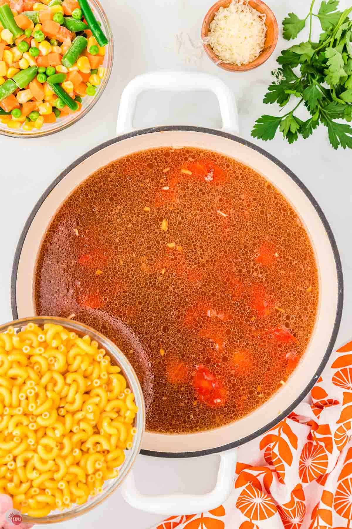 pot of tomato broth with raw macaroni noodles being poured in