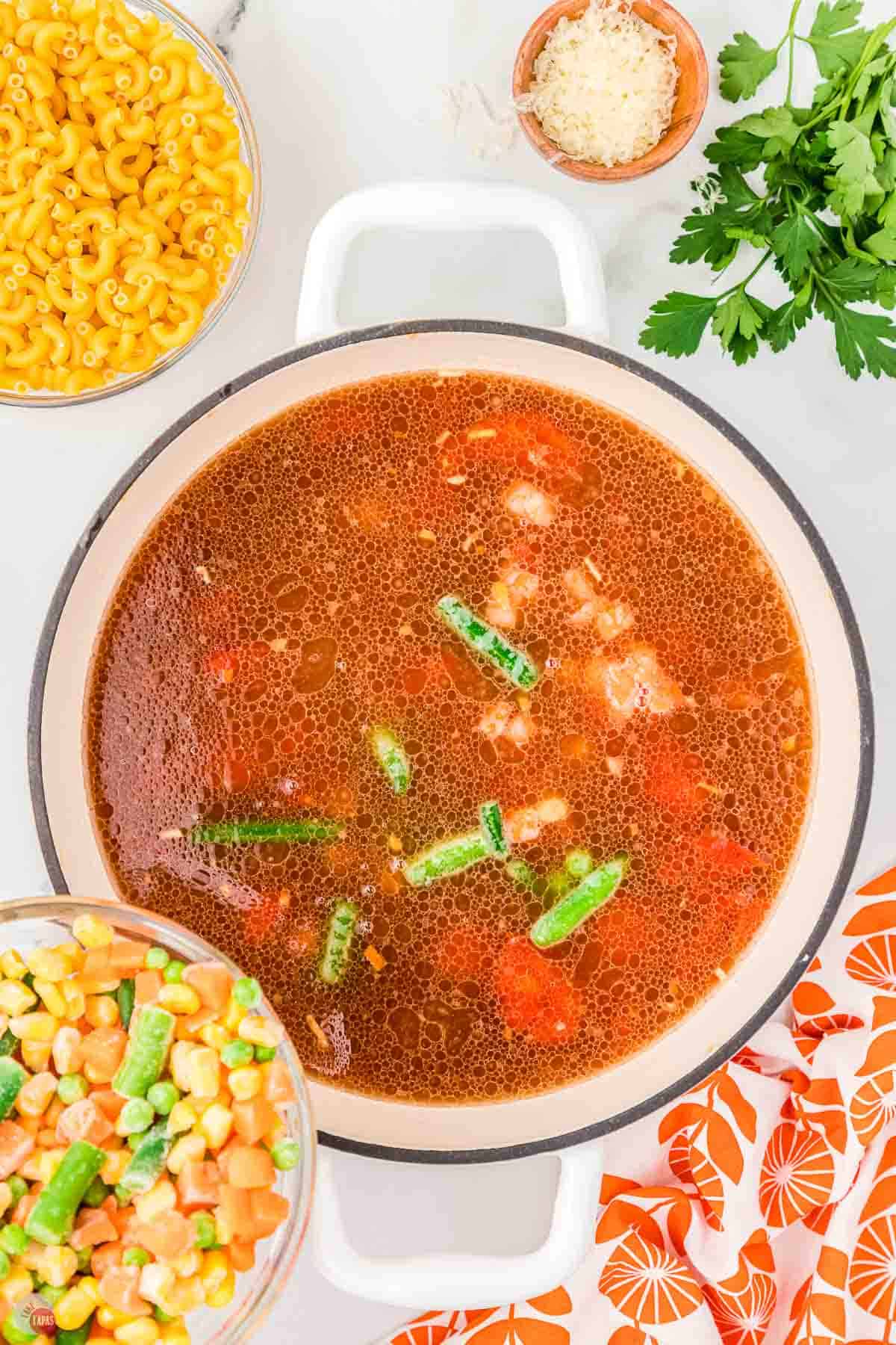 tomato soup in a pot with frozen vegetables being poured in