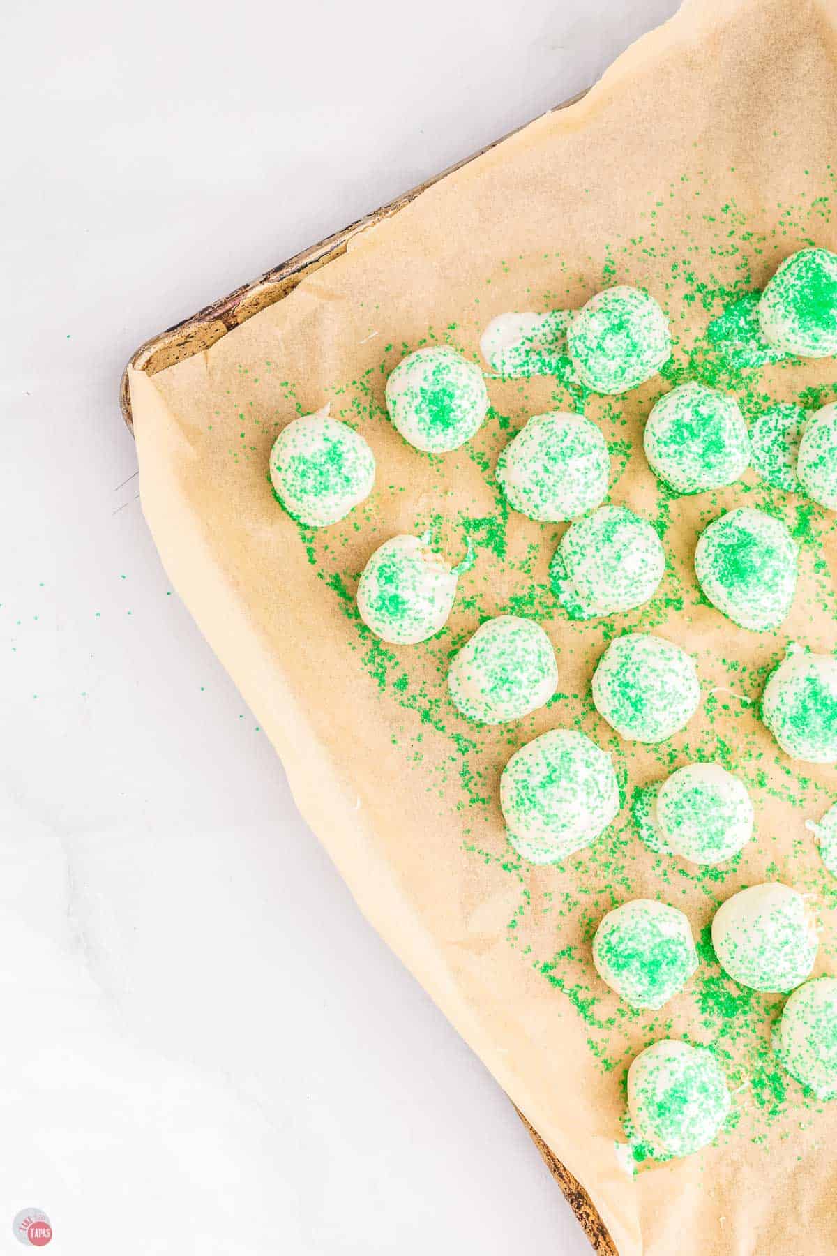 white cake balls on a baking sheet covered with green sprinkles