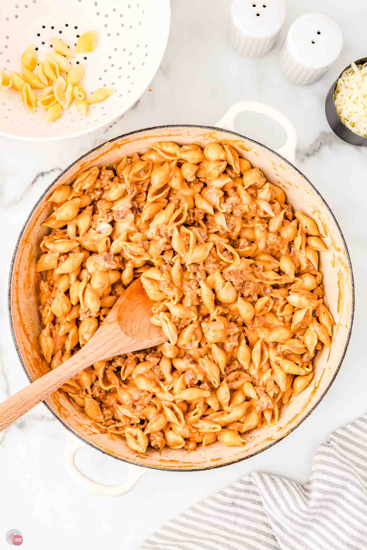 wood spoon stirring sour cream into beef and shells in a skillet