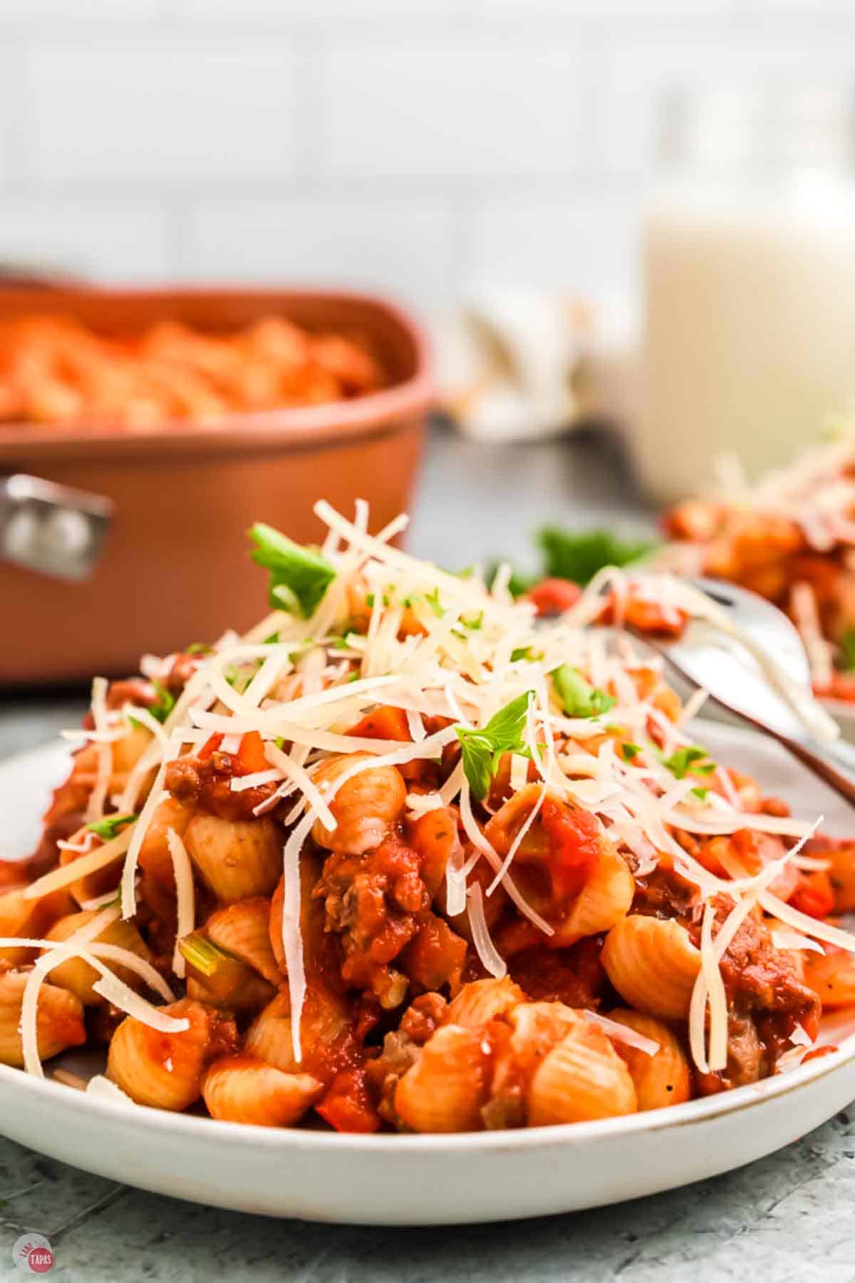 close of up beefaroni topped with cheese on a plate with a skillet in the background