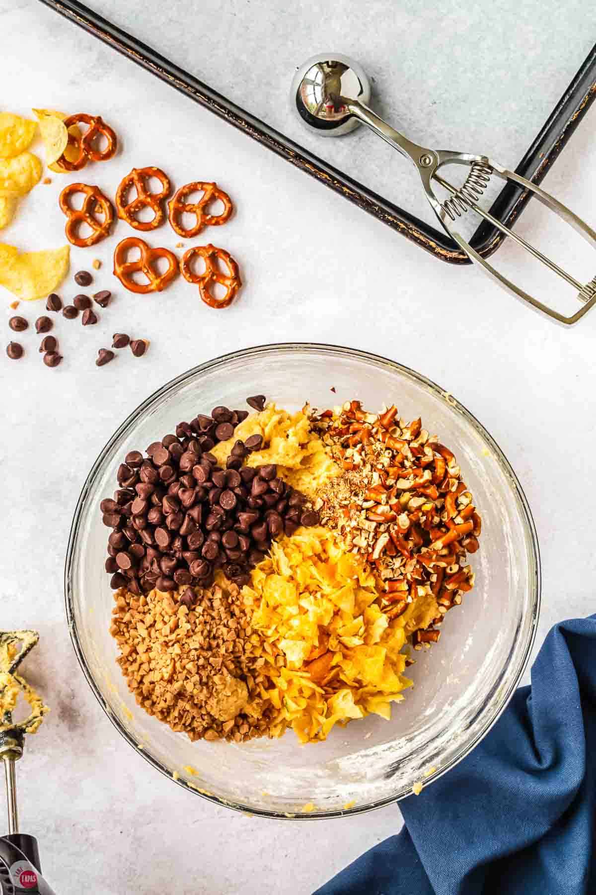cookie dough in a clear bowl topped with chocolate chips and pretzels