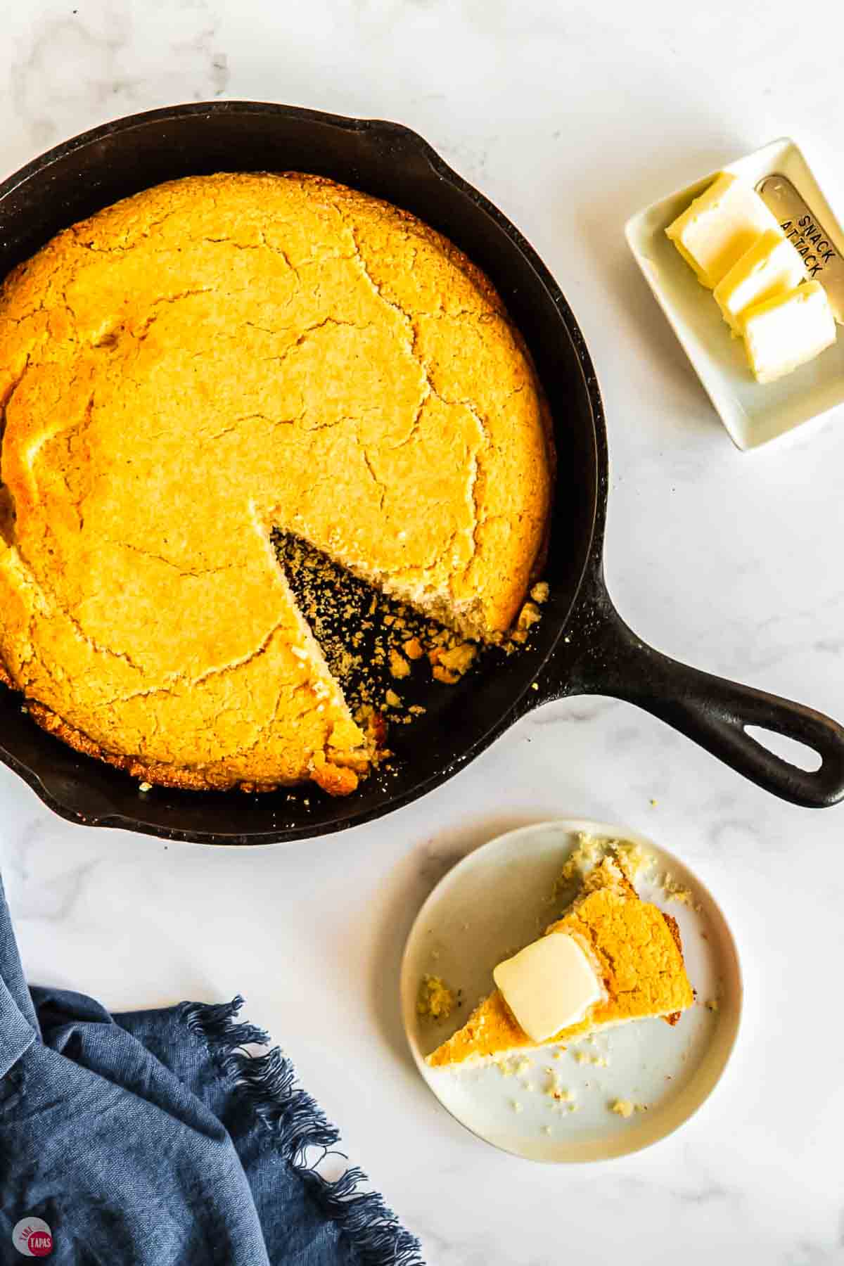 skillet of cornbread with plate next to it and a pat of butter on top